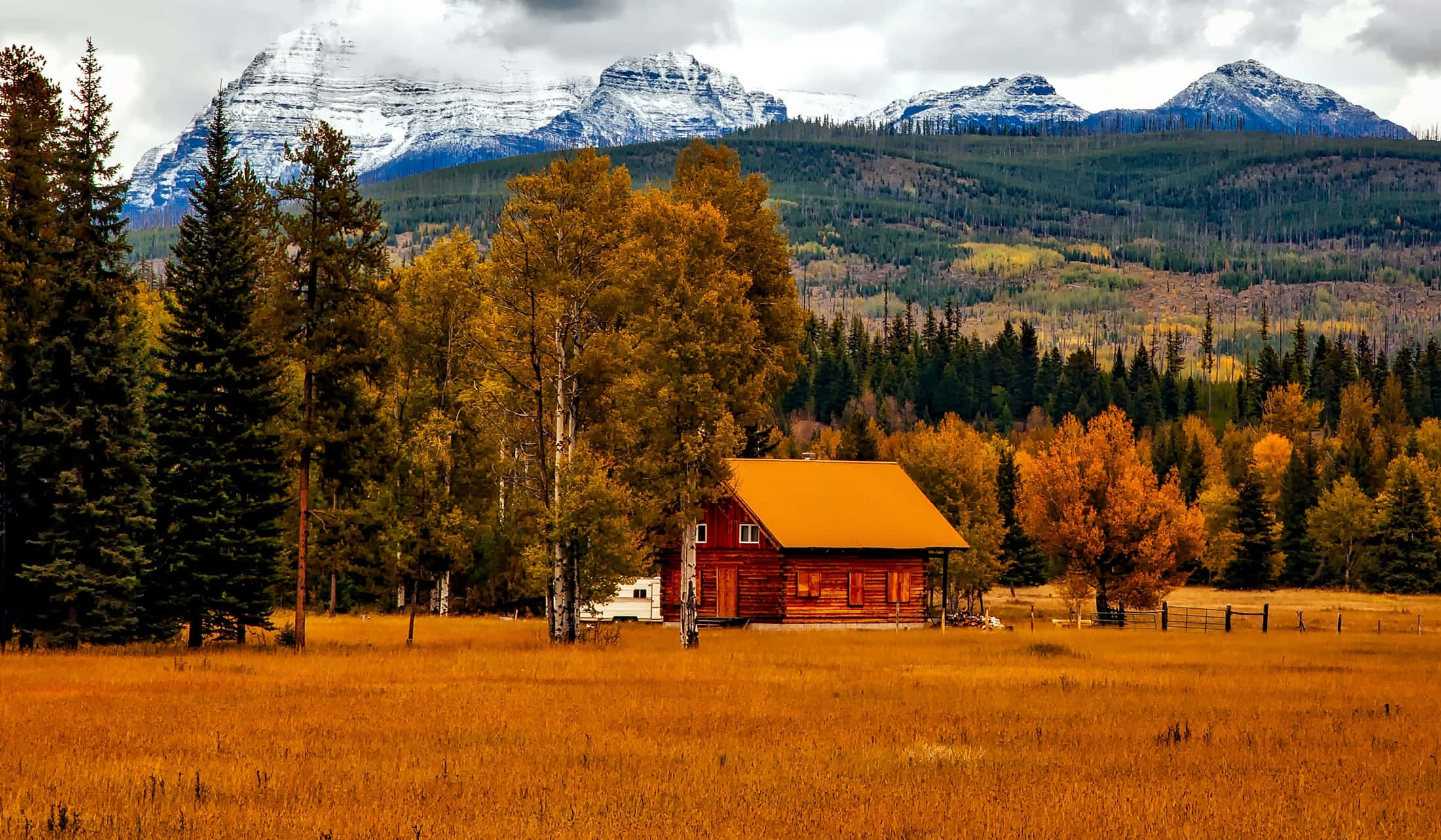 Colorado 桌布 壁紙 — 一間質樸的紅色小屋坐落在金色的田野中，背景有秋天的樹木和白雪覆蓋的山峰。