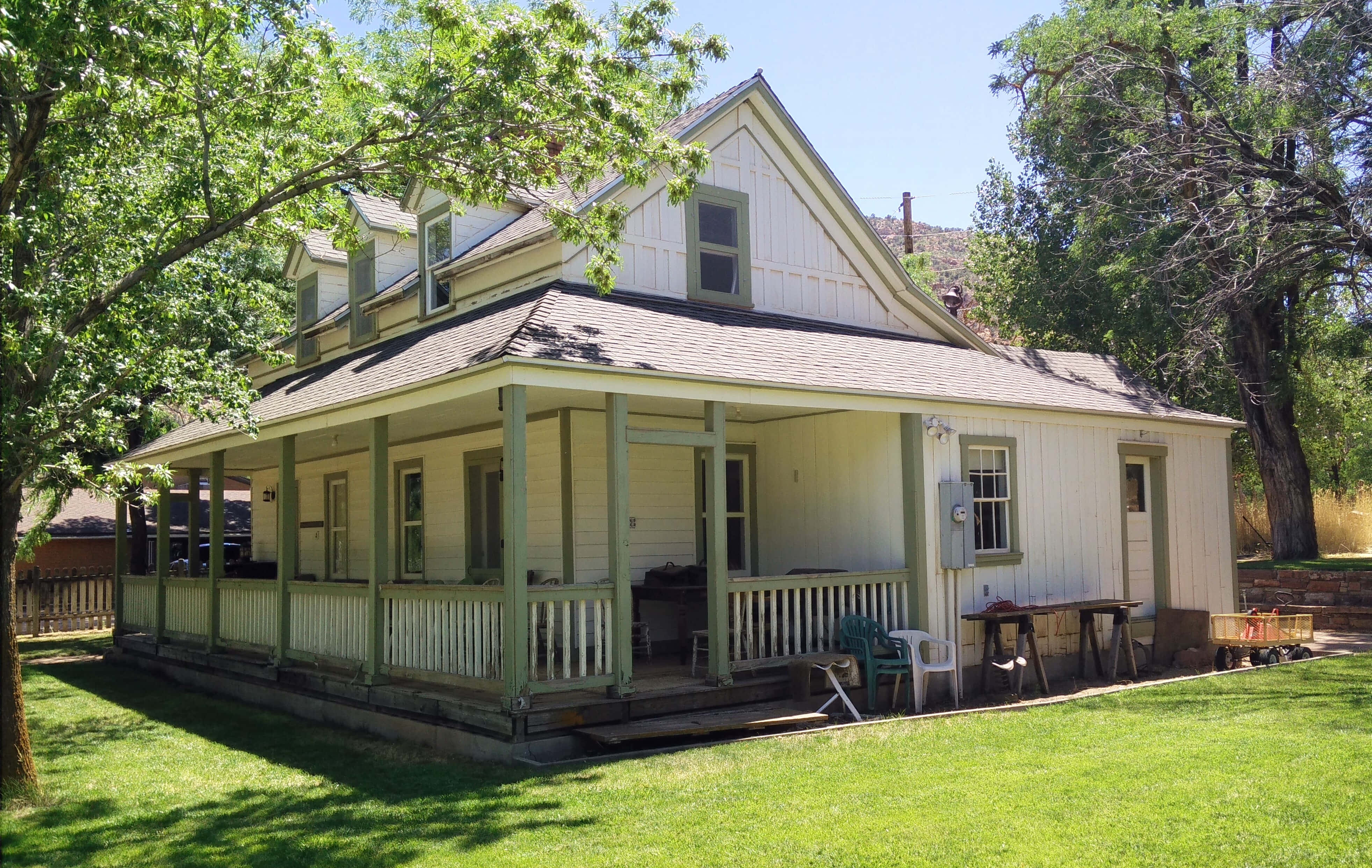 Big House 桌布 壁紙 — 一間迷人的白色木板屋，帶有綠色飾邊和環繞式門廊，坐落於陽光普照的草地上，周圍環繞著成熟的樹木。