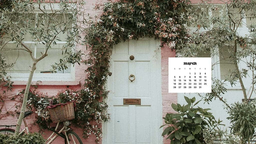 March Desktop 桌布 壁紙 — 一間迷人的粉紅色房子，帶有白色門，門上裝飾著盛開的藤蔓，旁邊停著一輛自行車。