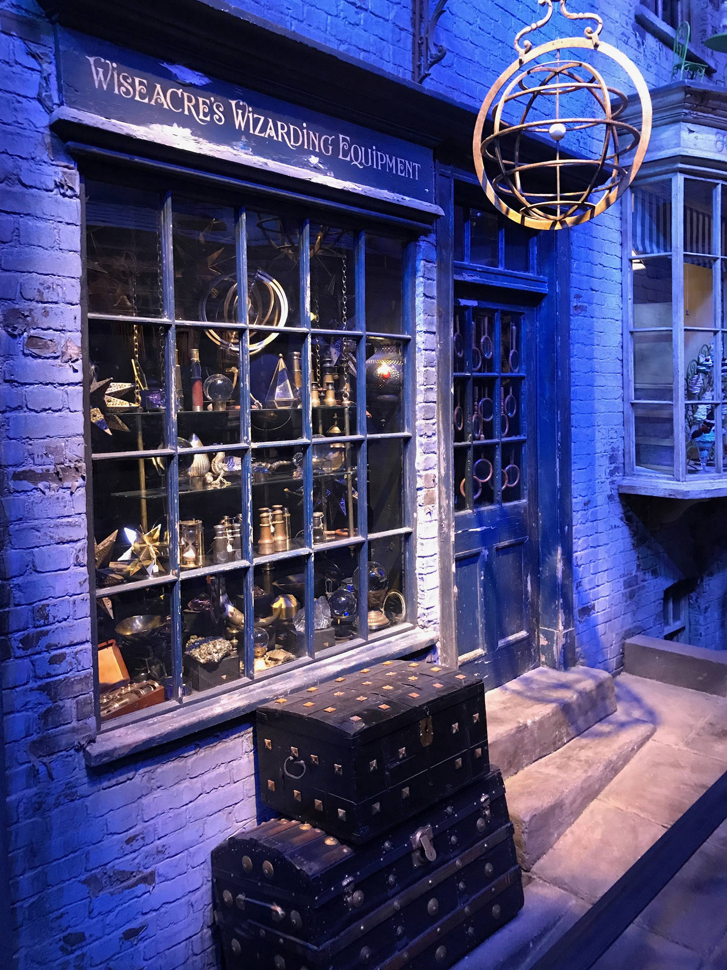 夜晚的Wiseacre's Wizarding Equipment商店，藍色燈光和堆疊的行李箱。 — 哈利波特 iPhone 壁紙 壁紙