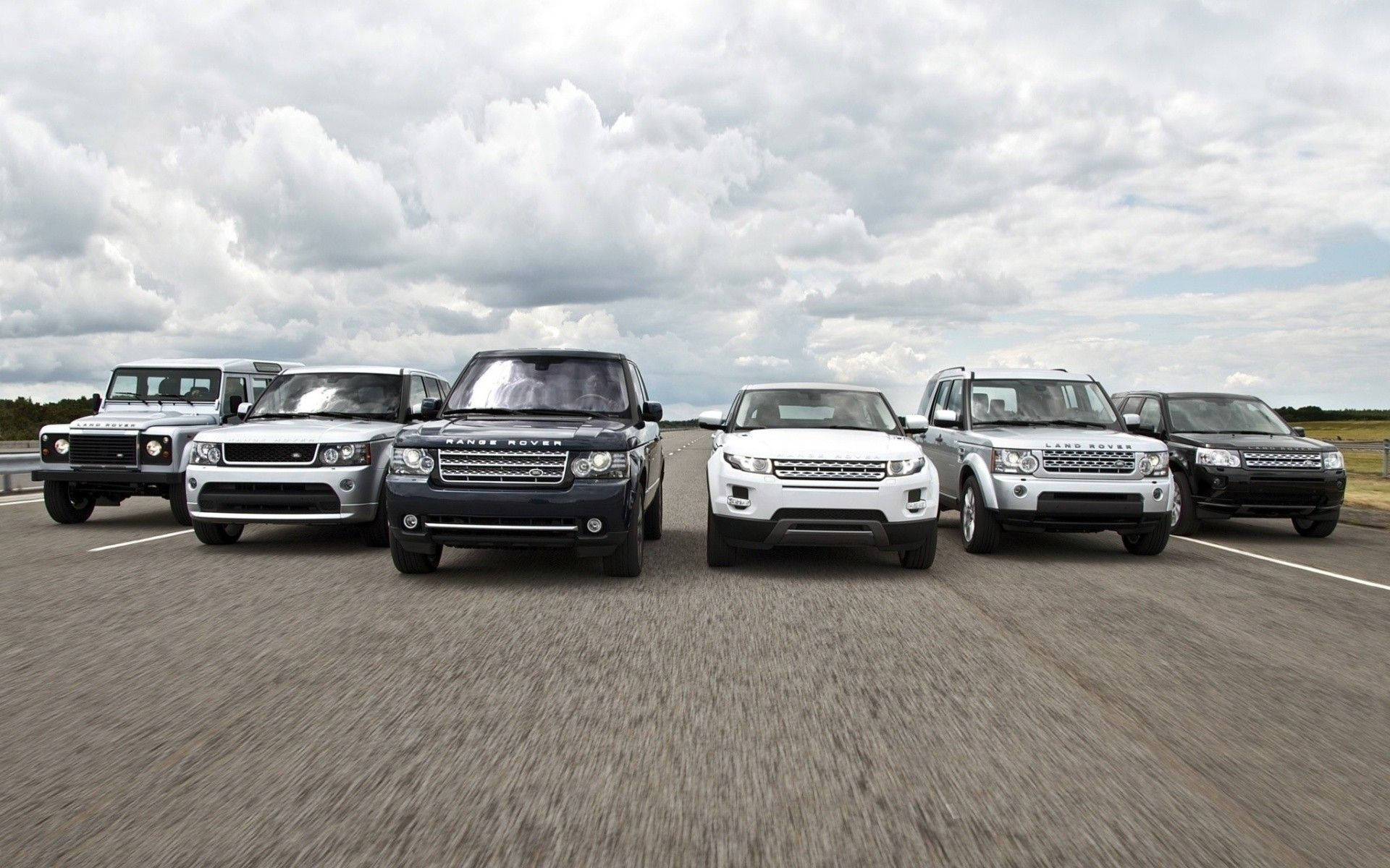 六輛 Land Rover SUV 在陰天的道路旁並排停放。