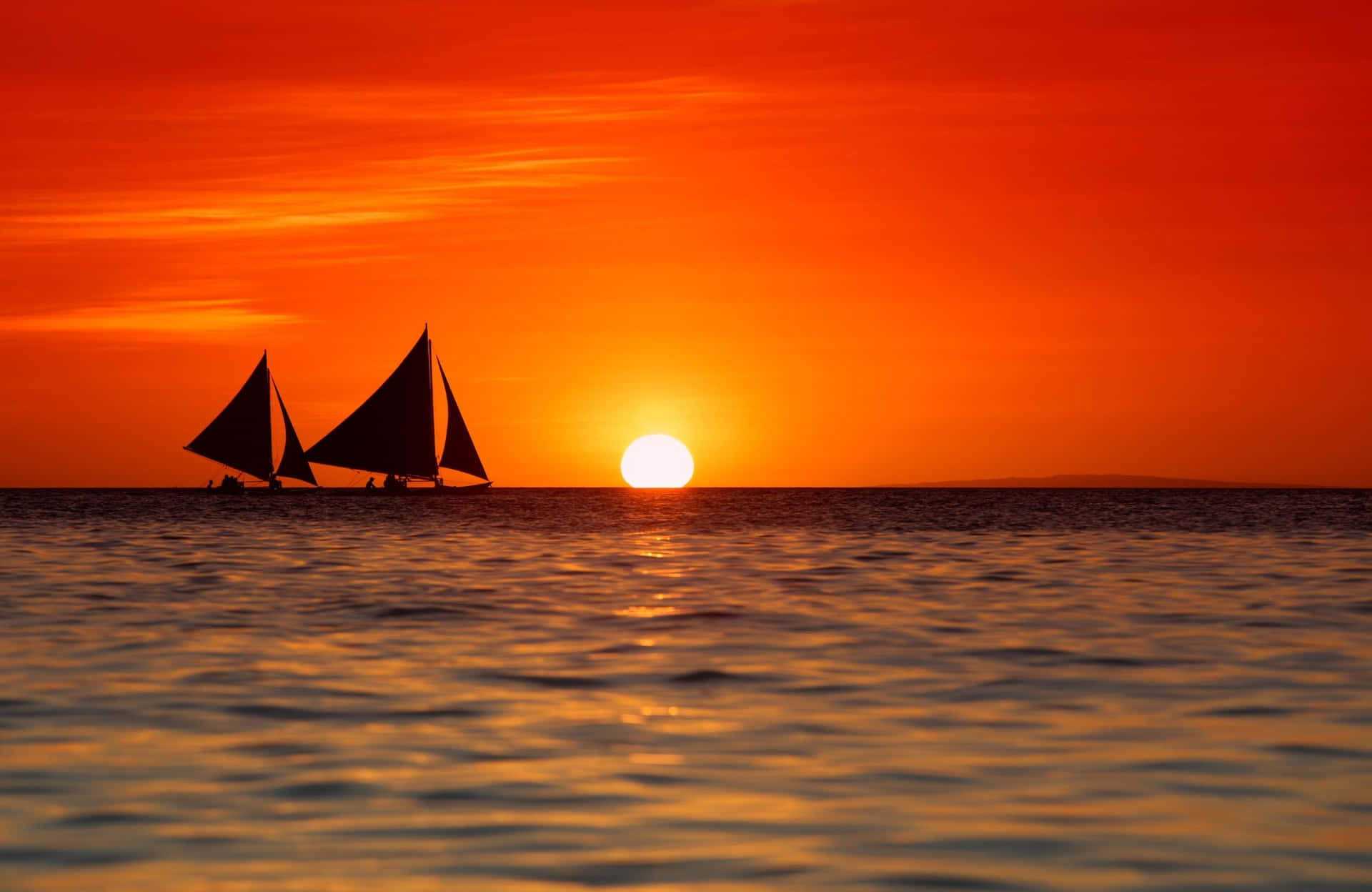 兩艘帆船在平靜的水面上，以鮮豔的橙色夕陽為背景形成剪影。