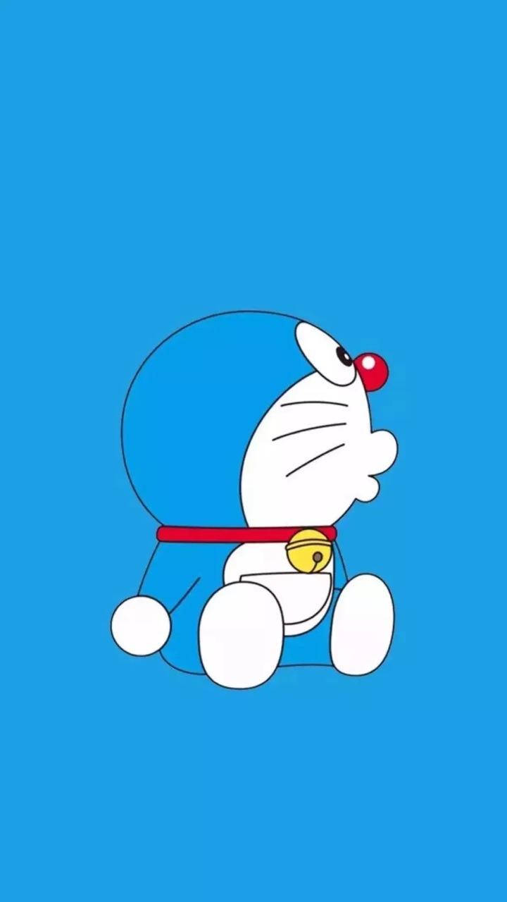 Doraemon 桌布 壁紙 — 一隻卡通機械貓，紅鼻子，掛著鈴鐺，坐在純藍色背景前。