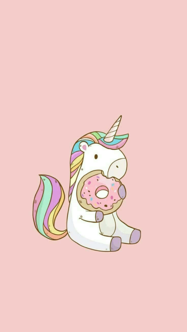 Cute Donut 桌布 壁紙 — 一隻可愛的卡通獨角獸，擁有彩虹鬃毛和尾巴，坐在柔和的粉紅色背景前，拿著一個粉紅色糖霜甜甜圈。