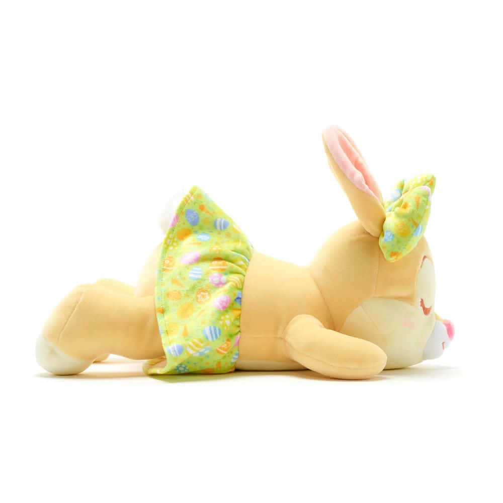 Miss Rabbit 桌布 壁紙 — 一隻可愛的黃色毛絨兔子側躺著，穿著綠色復活節蛋圖案的裙子和相配的蝴蝶結。