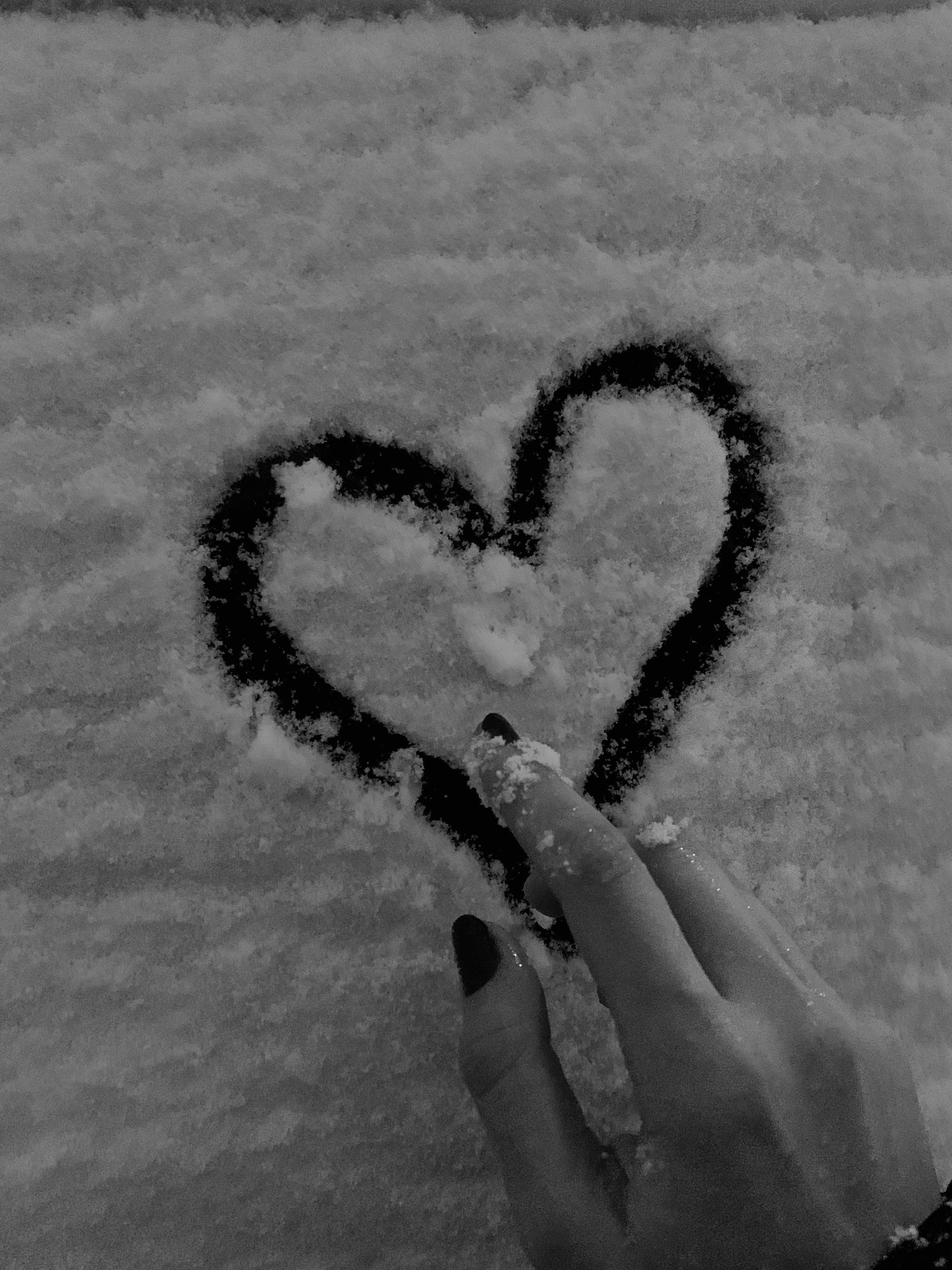心形 桌布 壁紙 — 一隻塗上深色指甲油的手在初雪中畫出心形，以單色和柔和質感捕捉。
