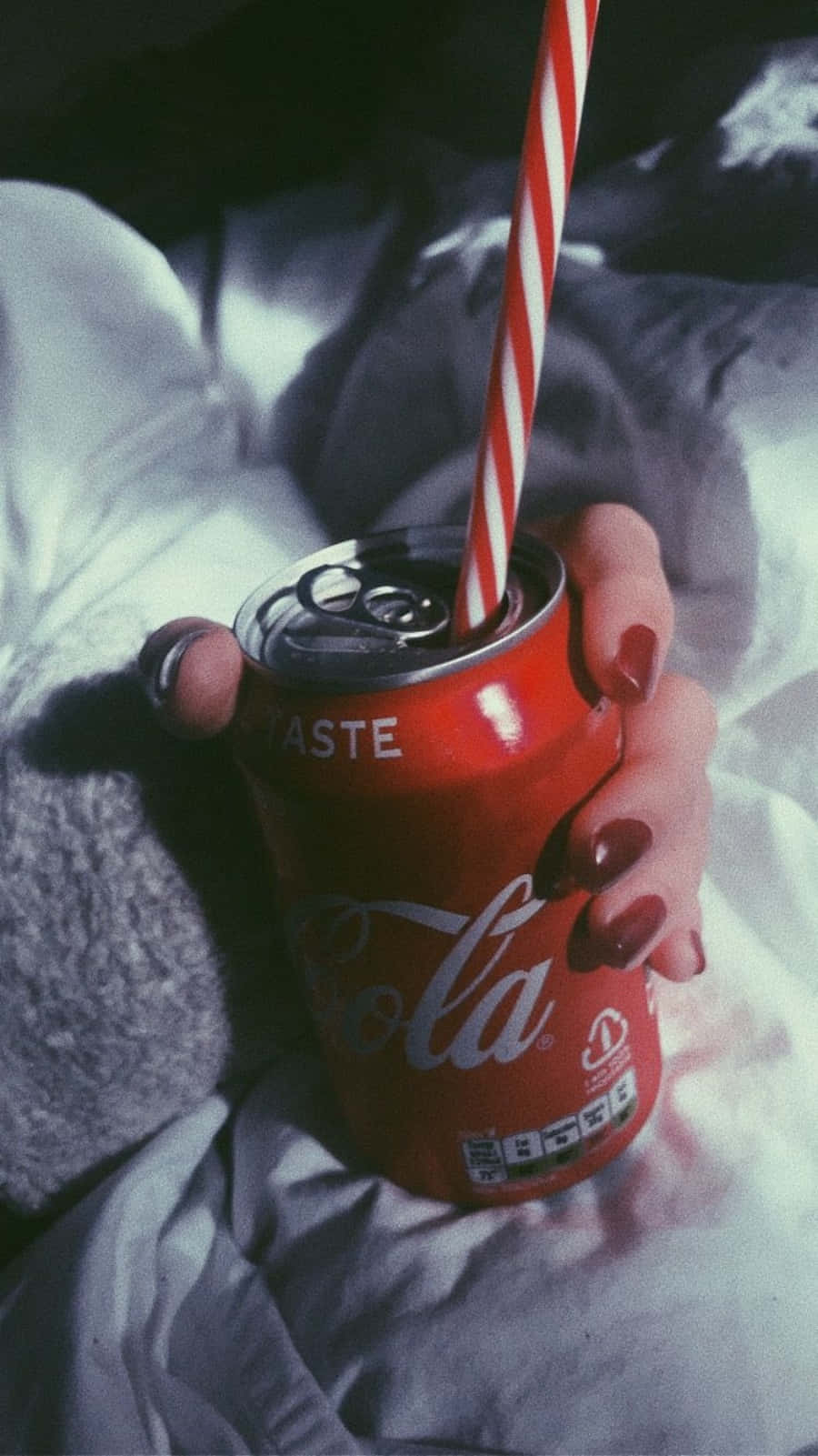 coca cola 桌布 壁紙 — 一隻塗有紅色指甲的手拿著一個紅色可口可樂罐，罐上插著紅白間條飲管，背景是皺巴巴的白色床單。
