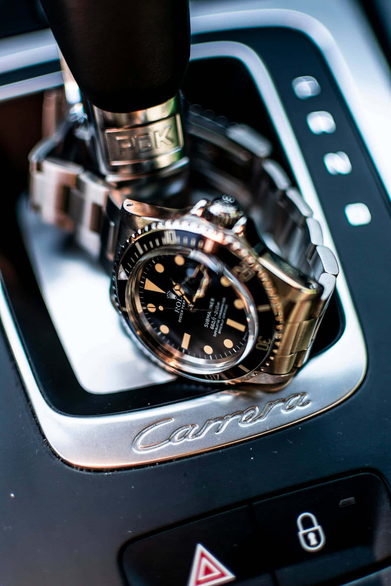 Rolex 桌布 壁紙 — 一隻奢華的勞力士Submariner手錶放在流線型銀色保時捷Carrera波棍上，周圍是汽車控制裝置。