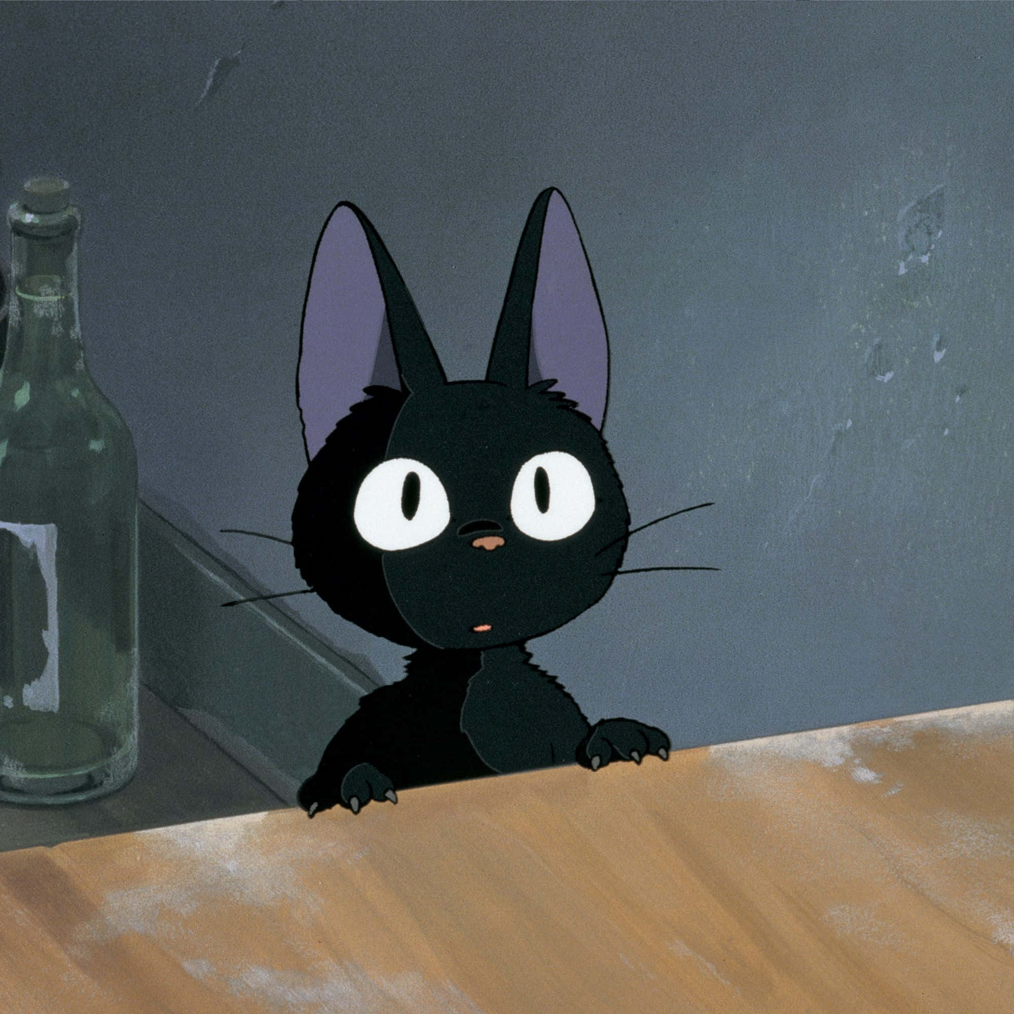 Jiji Cat 桌布 壁紙 — 一隻好奇的黑貓，有著白色大眼睛，從木質表面上方窺視，旁邊是一個佈滿灰塵的玻璃瓶，背景是灰色牆壁。