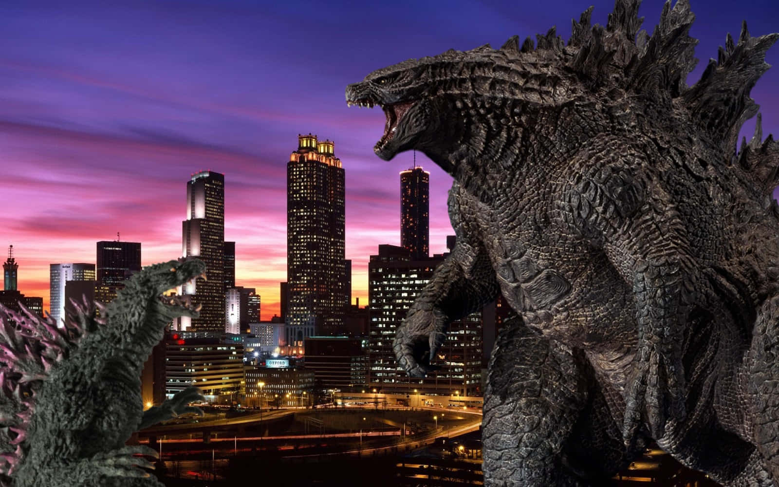 Godzilla 2000 桌布 壁紙 — 一隻巨大的哥斯拉在黃昏時分，於紫色和橙色天空下，對著發光的城市景觀咆哮。