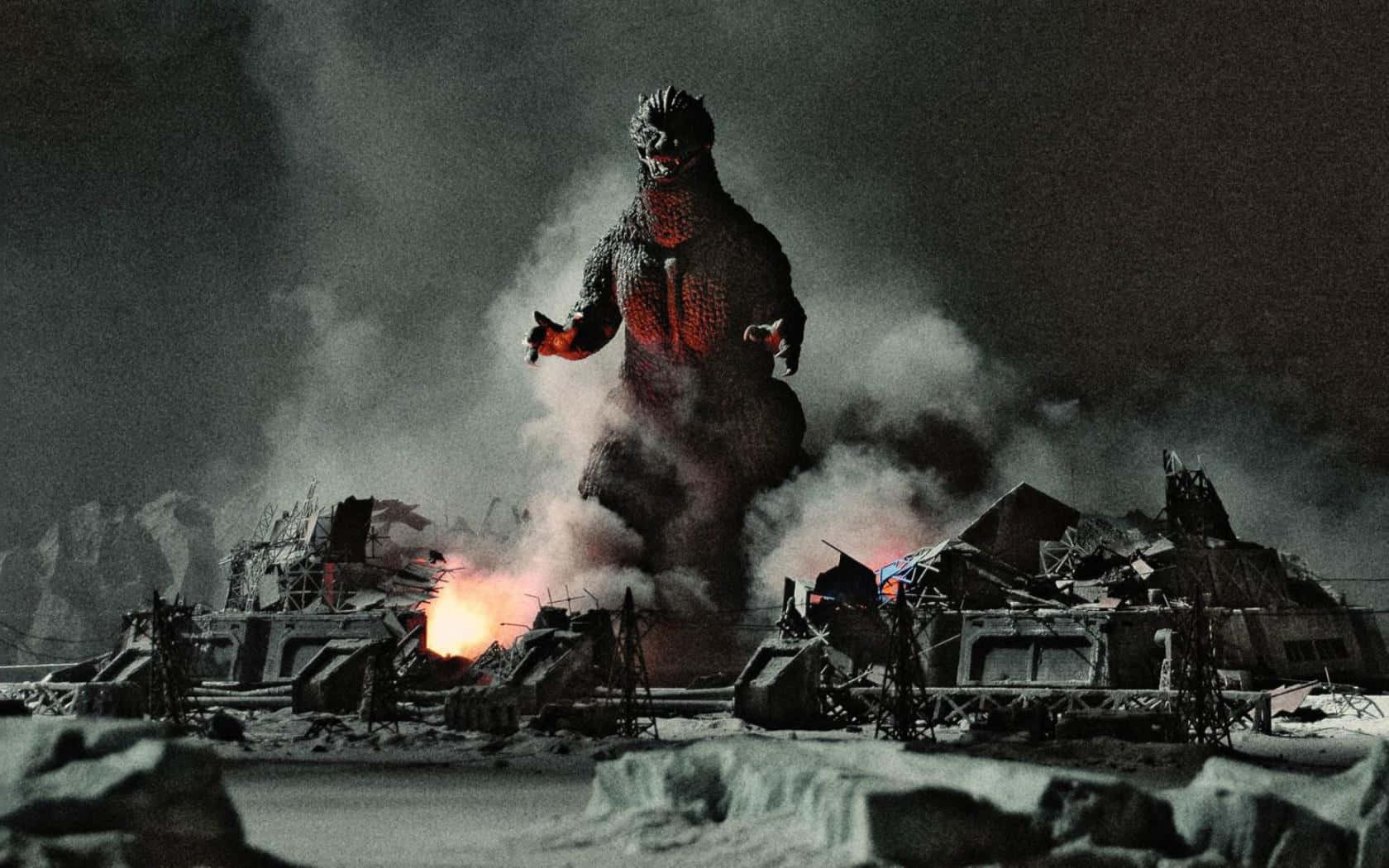 Godzilla 2000 桌布 壁紙 — 一隻巨大的哥斯拉站在被雪覆蓋的廢墟中，眼睛發出紅光，煙霧在其龐大的身軀周圍翻騰。