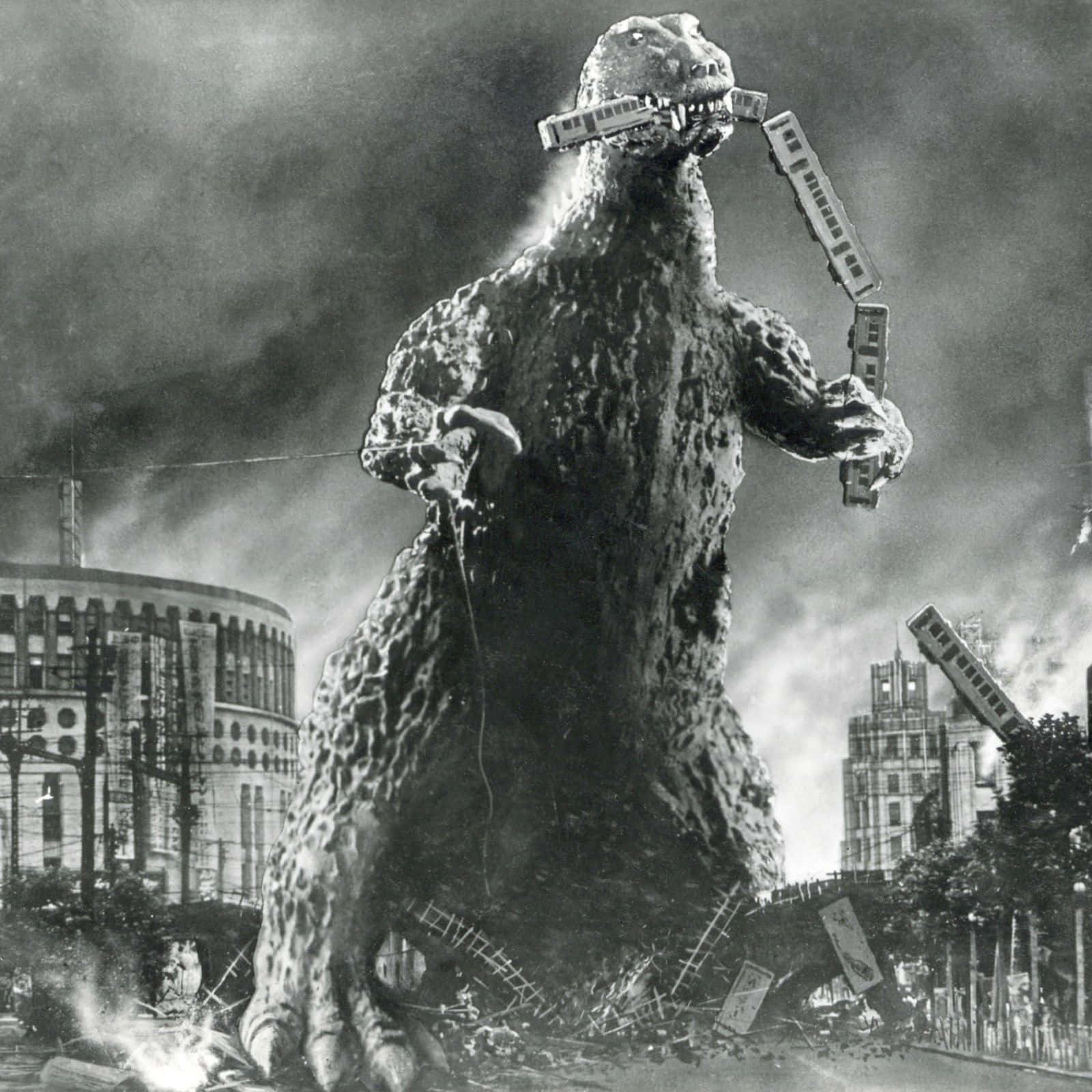 Godzilla 1954 桌布 壁紙 — 一隻巨大的怪獸嘴裡叼著火車車廂，站在煙霧瀰漫的天空下，廢墟般的城市景觀中。