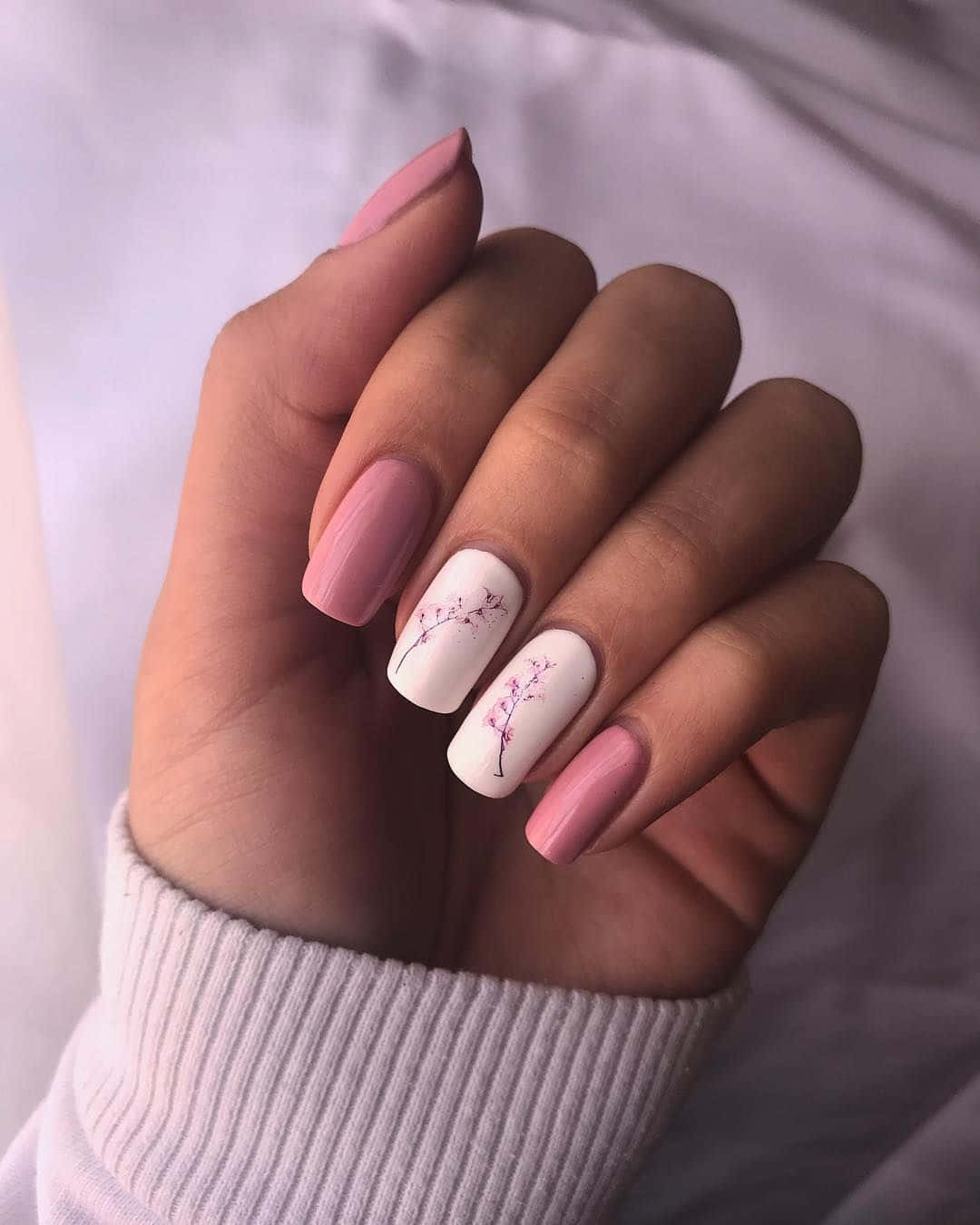 Spring Nails 桌布 壁紙 — 一隻帶有柔和粉紅色和白色指甲、飾有精緻櫻花圖案的手，輕輕地放在羅紋毛衣袖子上。