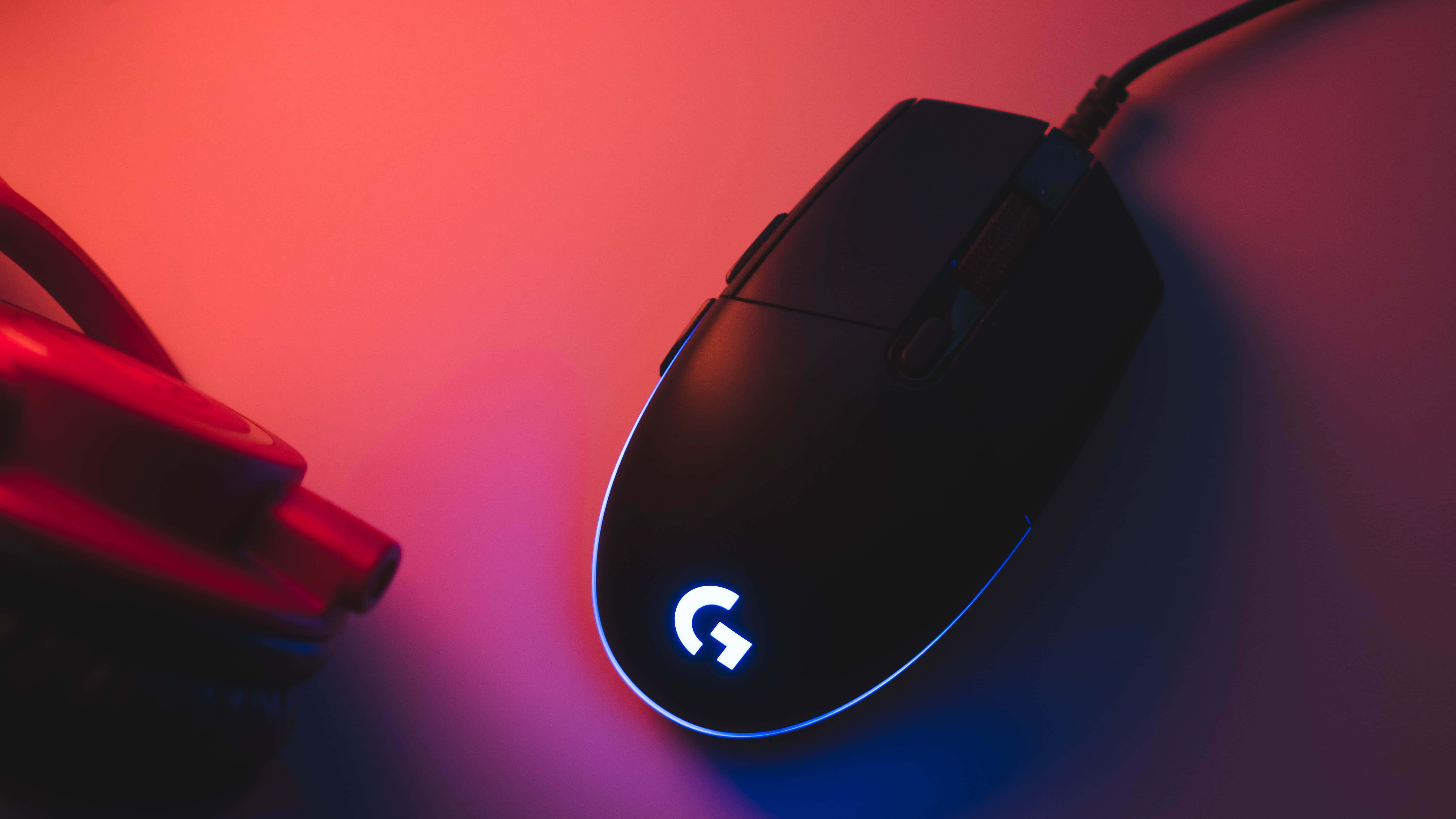 Gaming Mouse 桌布 壁紙 — 一隻帶有發光標誌的黑色Logitech遊戲滑鼠，放置在鮮豔的紅色和藍色霓虹燈下。