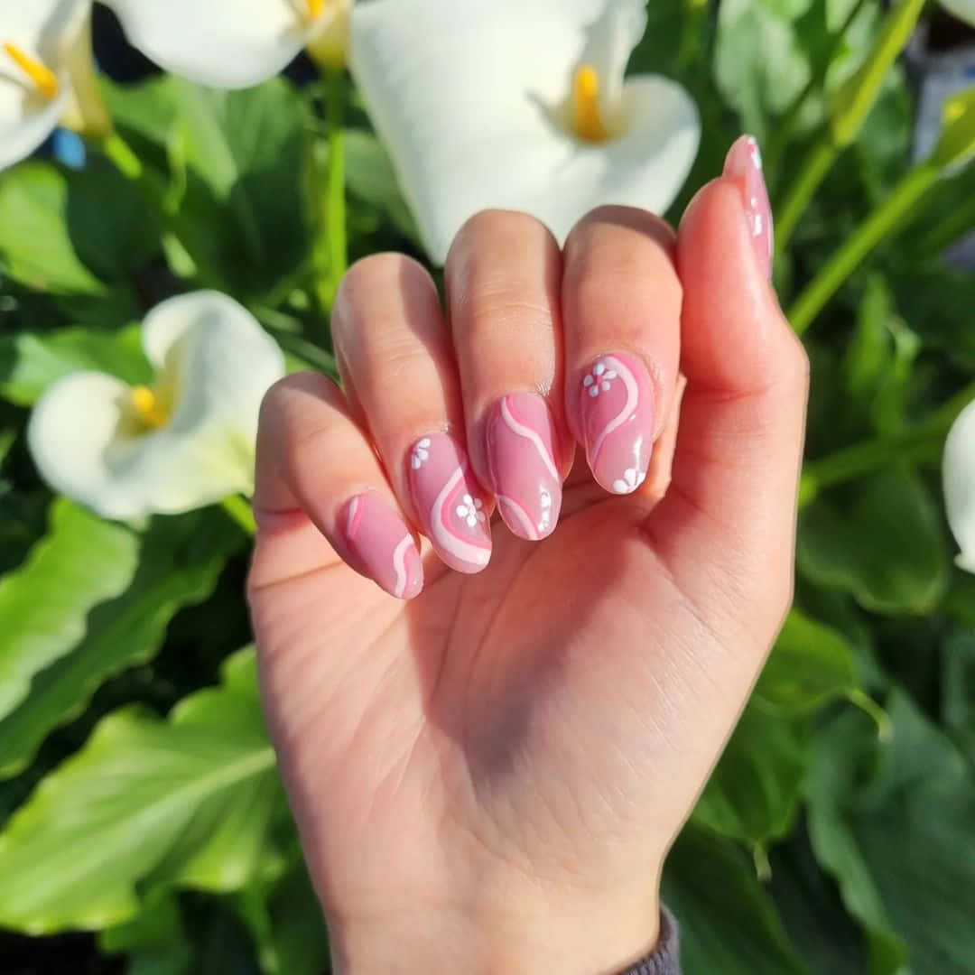 Pink Nail Art 桌布 壁紙 — 一隻帶有粉紅色花卉指甲的手輕輕放在白色馬蹄蓮和茂盛綠葉的背景上。