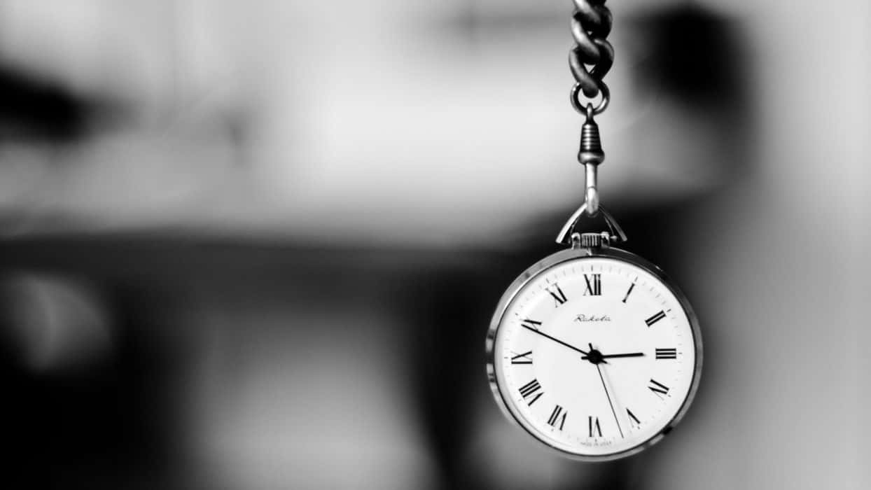 Time 桌布 壁紙 — 一隻帶有羅馬數字的復古懷錶，用鏈條懸掛在模糊的黑白背景前。