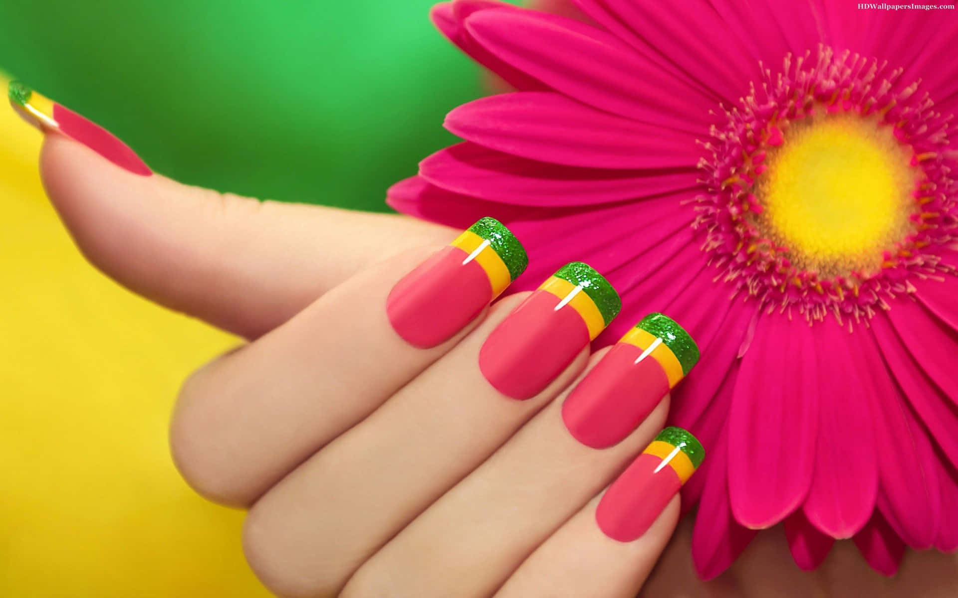 Pink Nails 桌布 壁紙 — 一隻帶有鮮豔粉紅色指甲並以綠色和黃色條紋點綴的手，輕輕握著一朵鮮粉紅色非洲菊雛菊，背景是色彩繽紛的綠色和黃色。