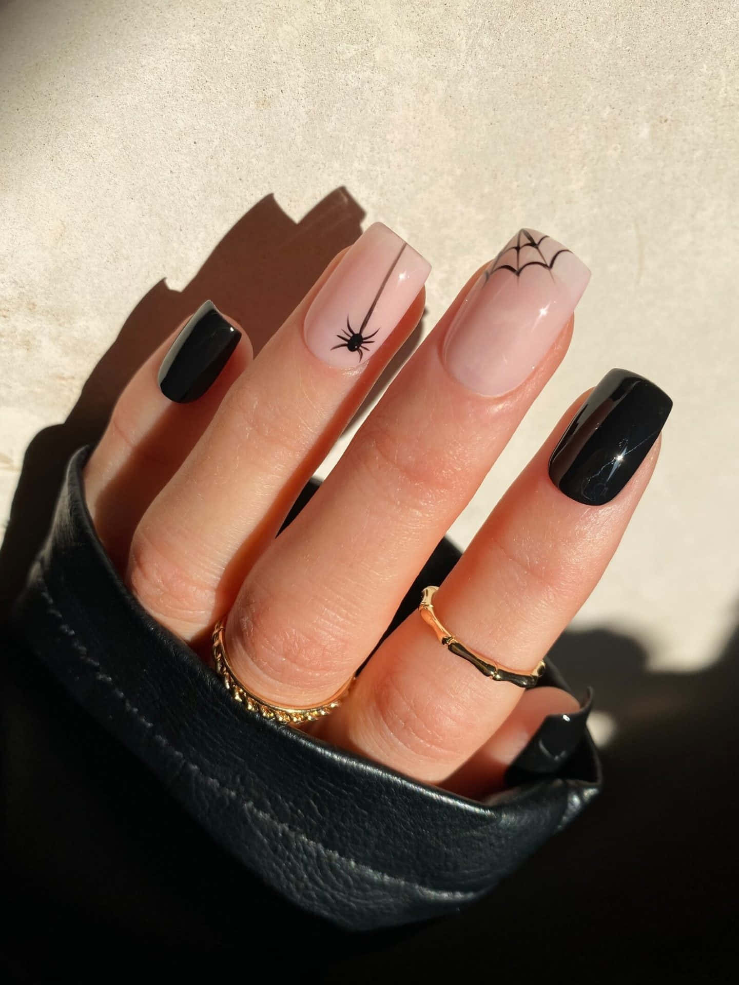 Halloween Nail Art 桌布 壁紙 — 一隻帶有黑色和裸色指甲、飾有蜘蛛網和蜘蛛圖案的手，在溫暖的陽光下放在黑色皮革袖口中。