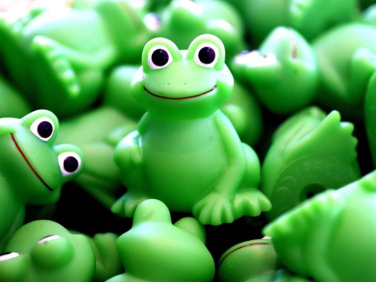 Aesthetic Frog 桌布 壁紙 — 一隻快樂的綠色塑膠青蛙玩具在柔焦中，在一片相同的青蛙海中燦爛微笑。