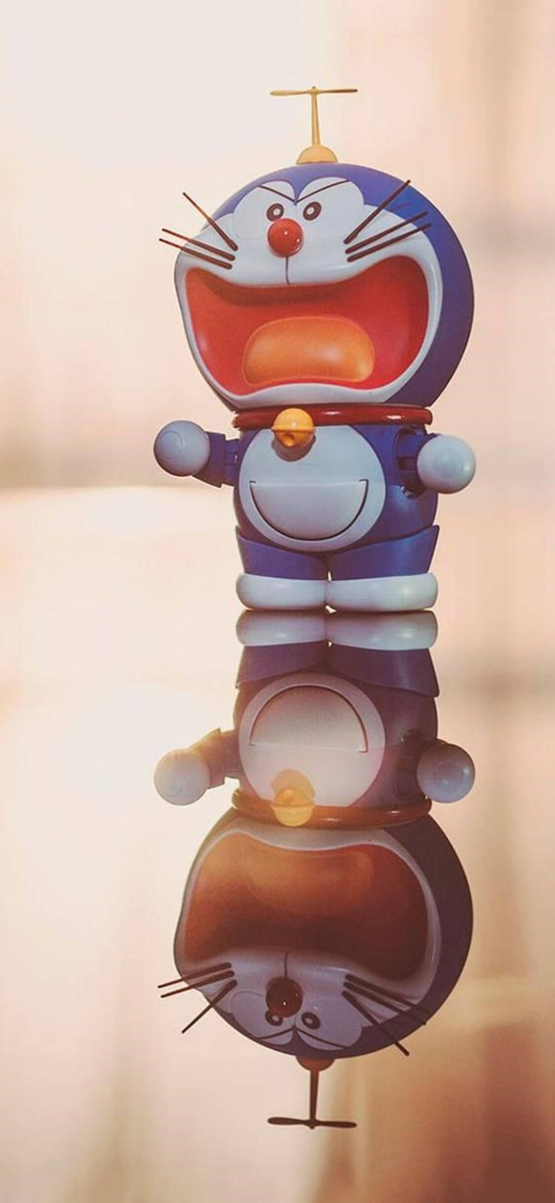 Doraemon 桌布 壁紙 — 一隻快樂的藍色機械貓，有紅色鼻子和天線，垂直堆疊，在光滑表面上倒映出上下顛倒的倒影。