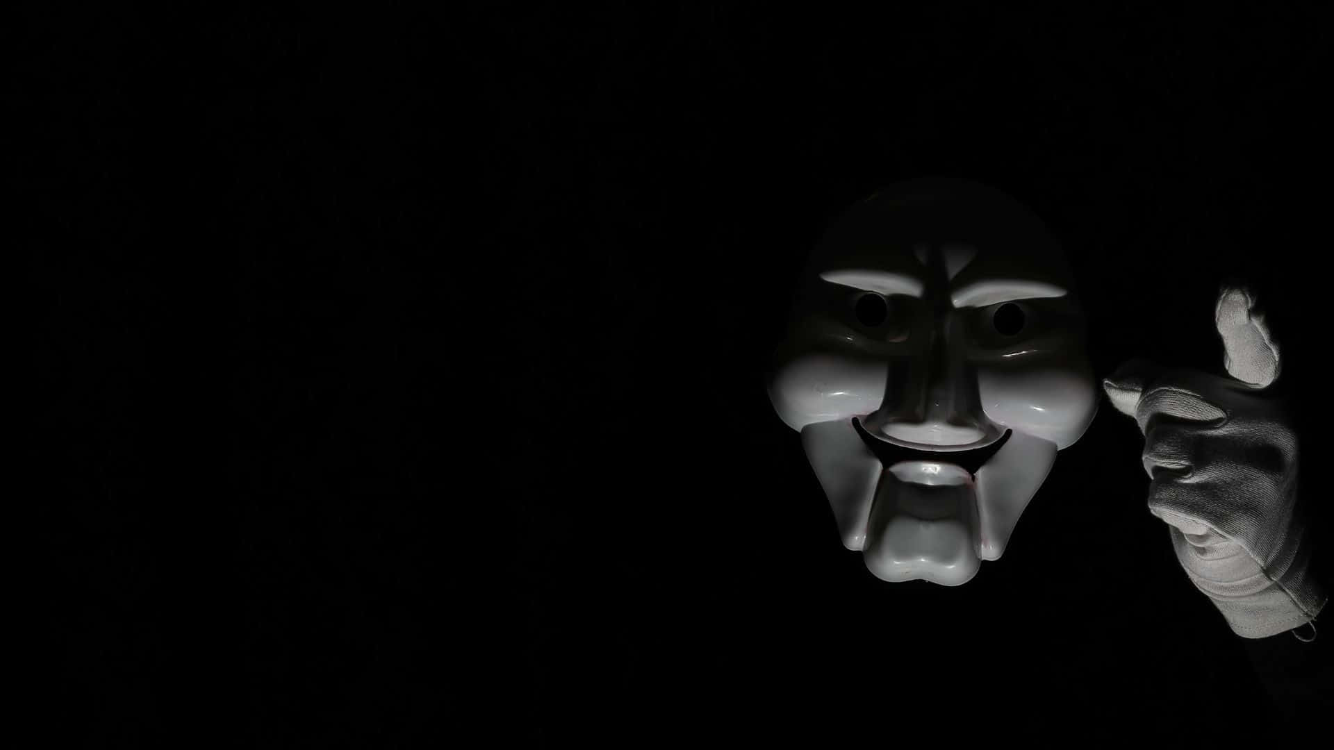 Horror Masks 桌布 壁紙 — 一隻戴手套的手在漆黑背景上，以戲劇性的聚光燈照射下，握著一個白色的蓋伊·福克斯面具。