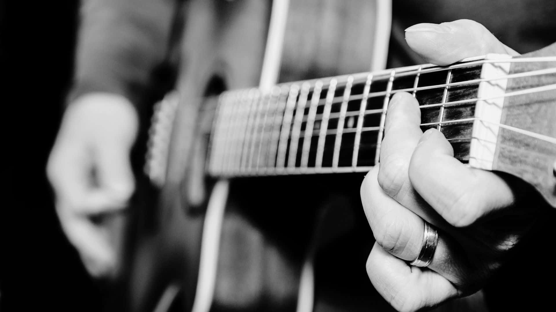 Black And White Guitar 桌布 壁紙 — 一隻戴著戒指的左手熟練地彈奏木結他的黑白特寫。