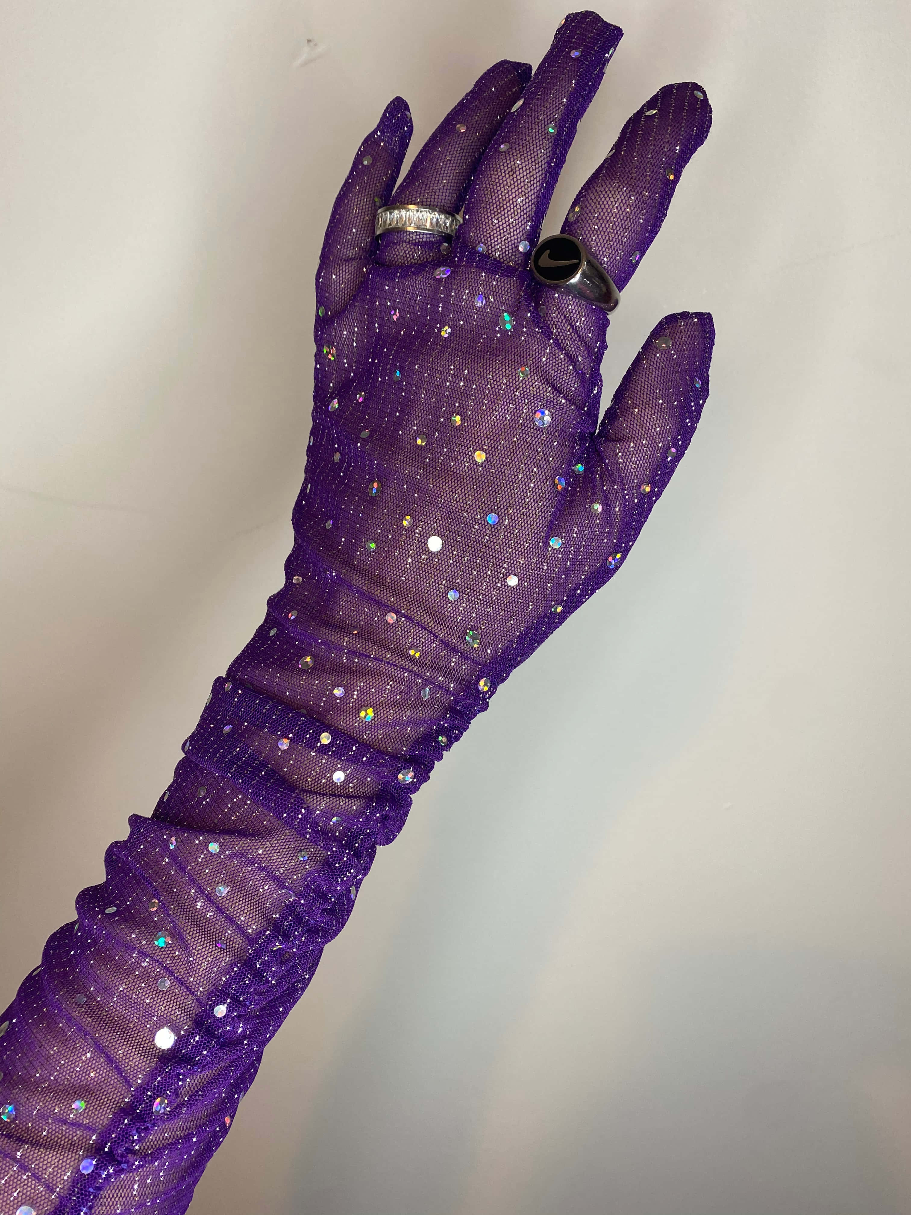 Purple Gloves 桌布 壁紙 — 一隻戴著閃亮紫色網狀手套的手，在純色背景上優雅地伸展，展示兩枚戒指。