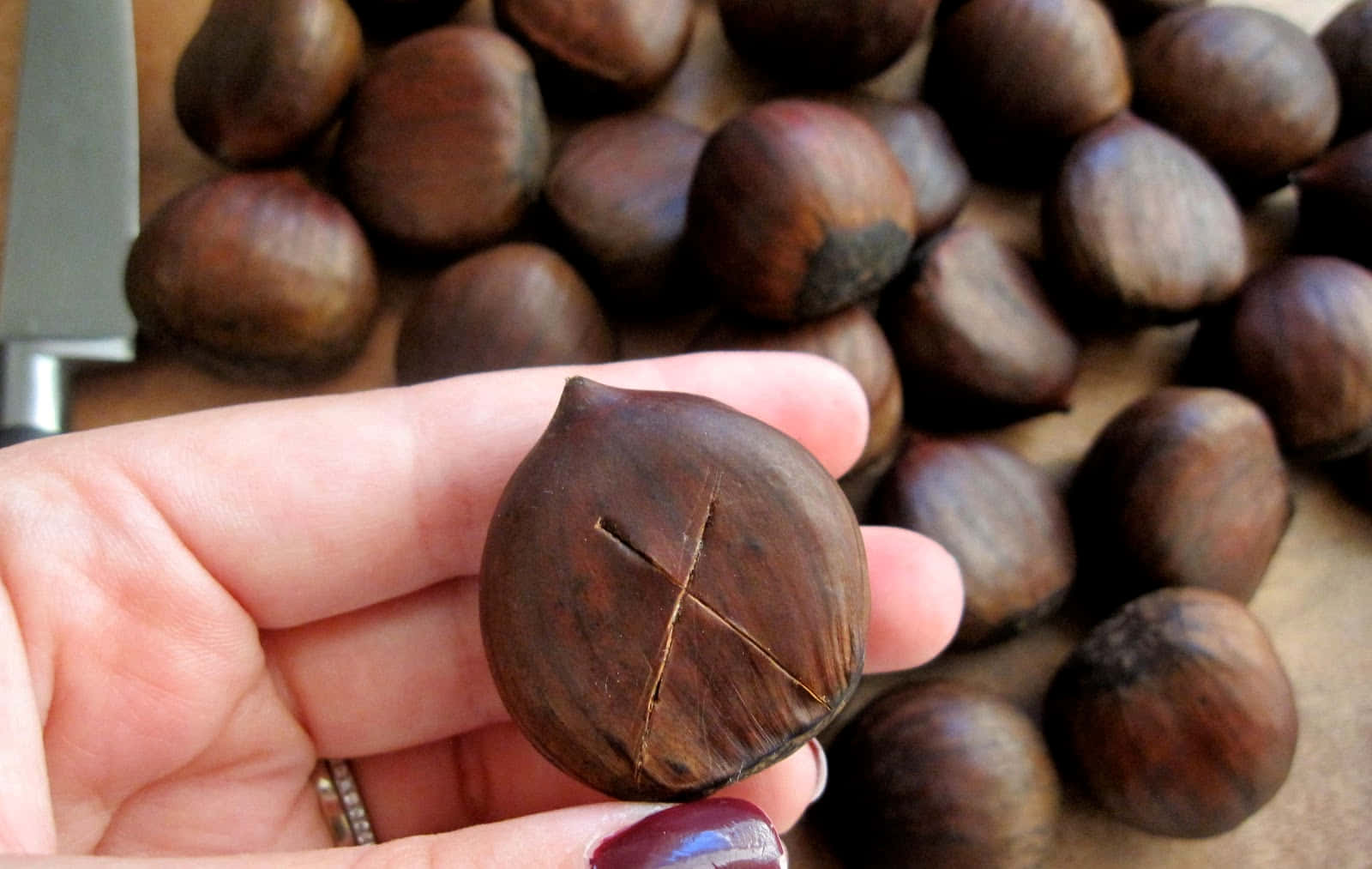 Chestnut 桌布 壁紙 — 一隻手喺一堆烤栗子上方拎住一個已劃開嘅栗子，附近有把刀。