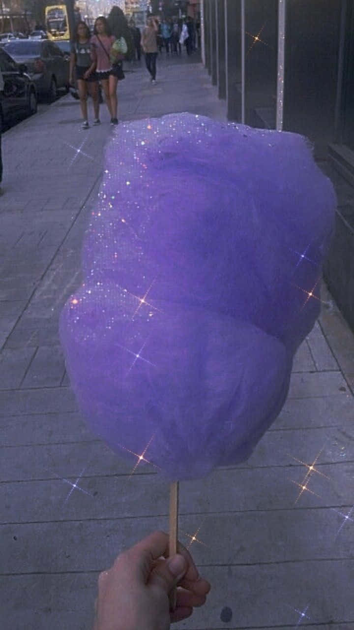 Purple Cotton 桌布 壁紙 — 一隻手喺城市行人路上，背景有行人同汽車，揸住一大支閃閃發光嘅紫色棉花糖。