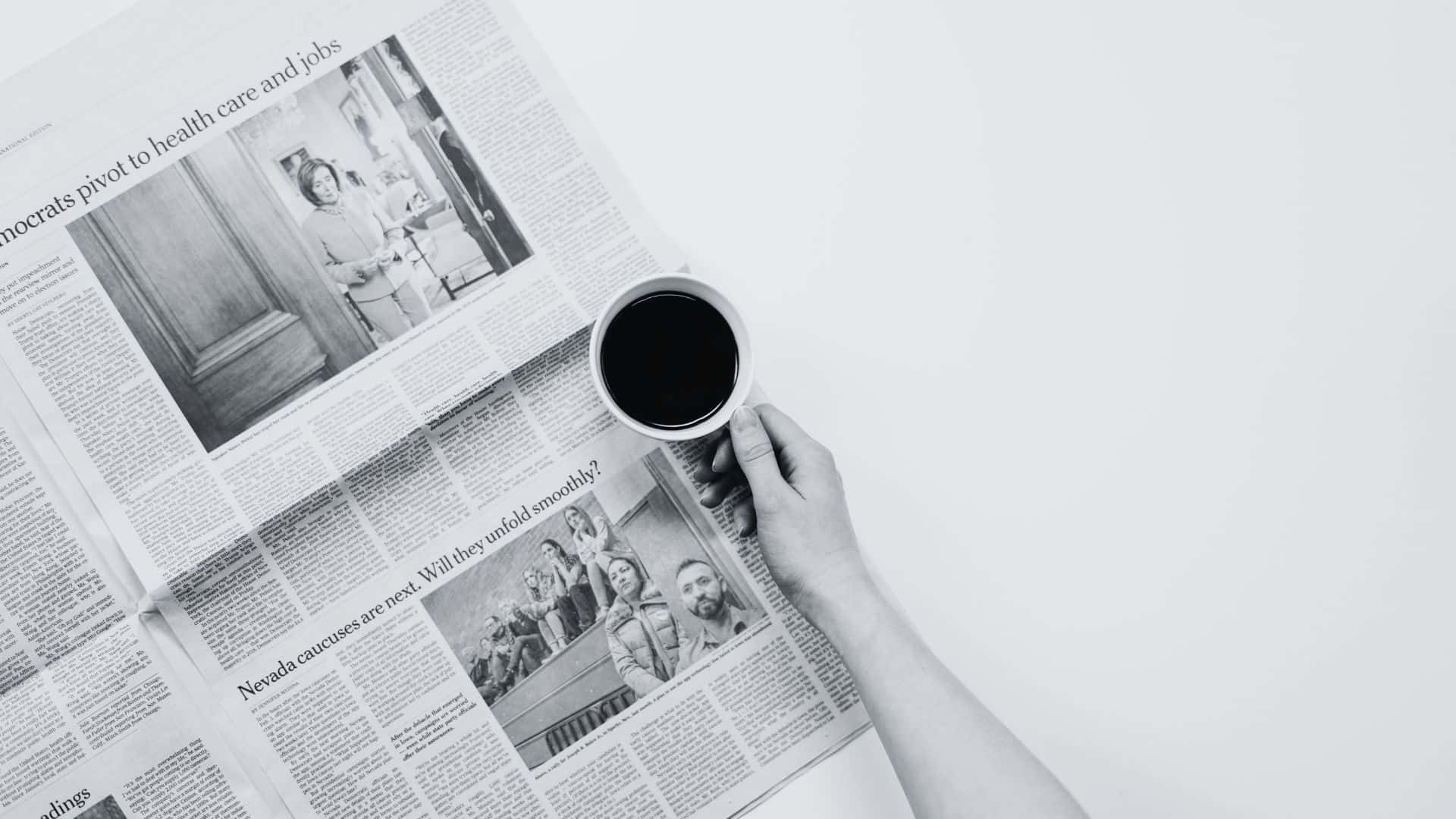 Black And White Newspaper 桌布 壁紙 — 一隻手喺極簡嘅單色俯拍鏡頭中，將咖啡杯拎喺散開嘅報紙標題上面。