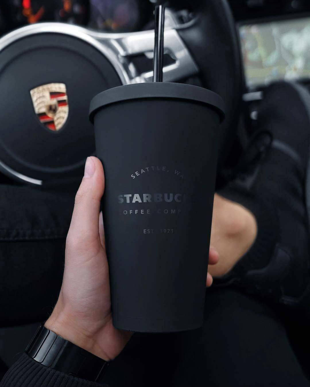 星巴克 桌布 壁紙 — 一隻手在保時捷內拿著一個啞光黑色的星巴克杯，方向盤上的標誌清晰可見。