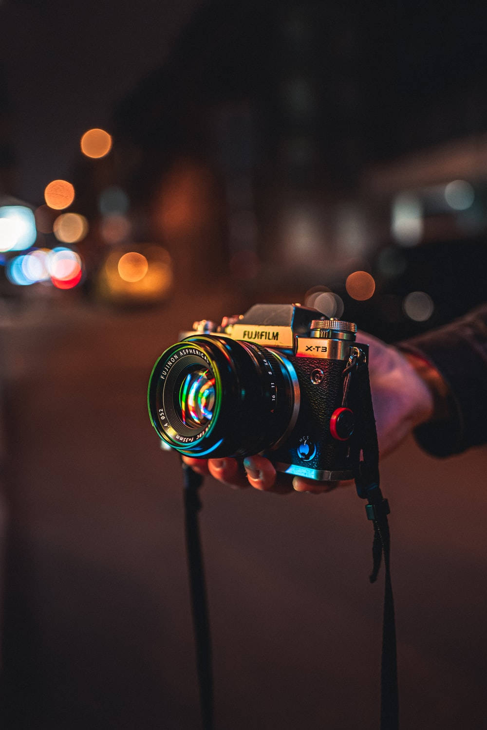 相機 桌布 壁紙 — 一隻手在夜晚拿著 Fujifilm X-T3 相機，背景是城市街道上色彩繽紛的散景燈光。
