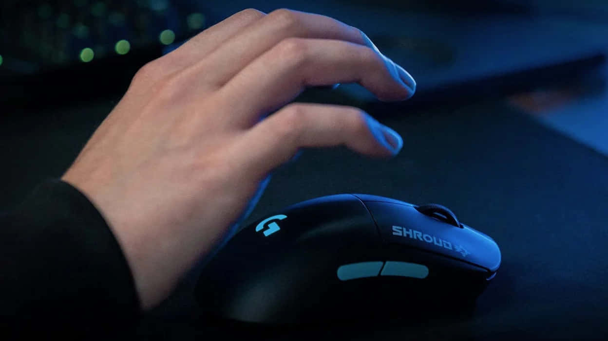 Gaming Mouse 桌布 壁紙 — 一隻手在昏暗的藍色燈光下握著一個帶有藍色發光裝飾的黑色電競滑鼠。
