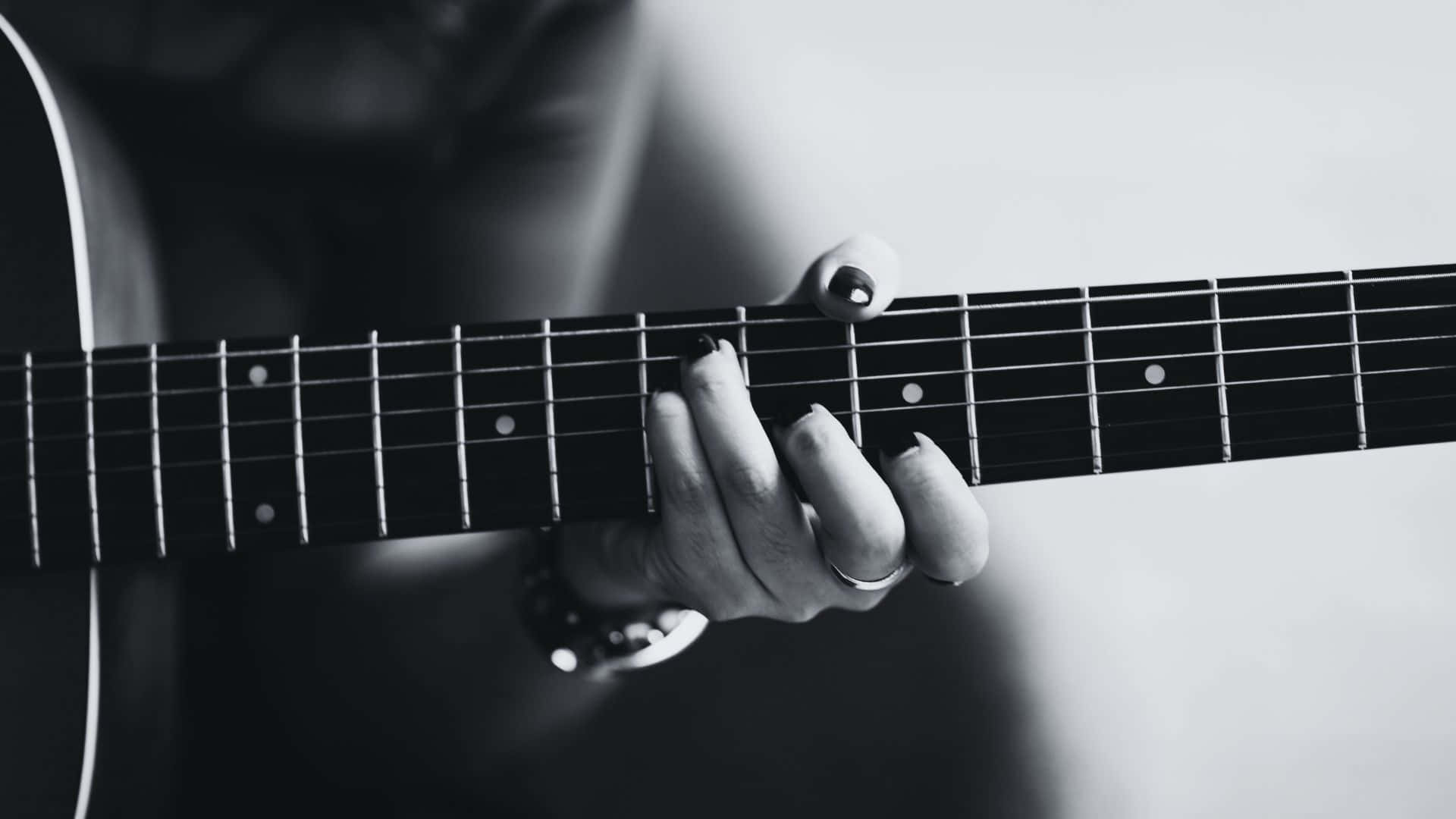Black And White Guitar 桌布 壁紙 — 一隻手在木結他指板上按弦的黑白特寫，戒指和手錶清晰可見。