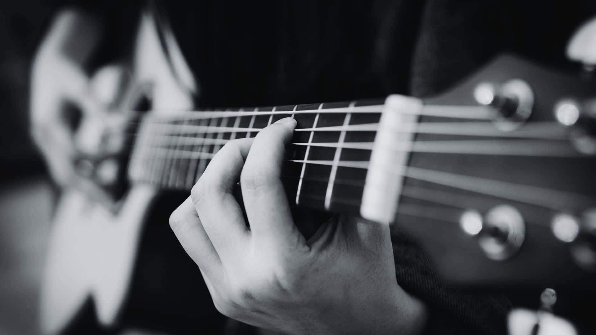 Black And White Guitar 桌布 壁紙 — 一隻手在木結他頸上按弦的黑白特寫，背景模糊。