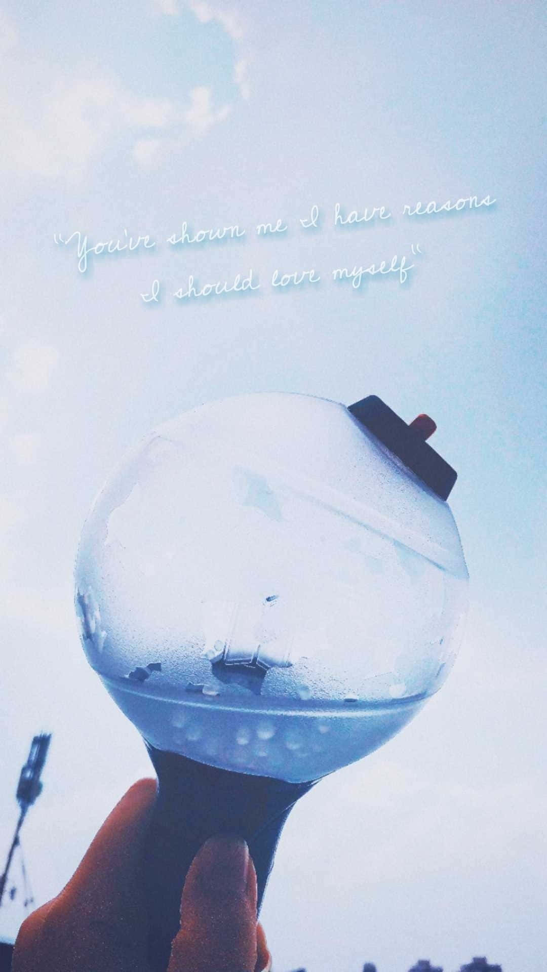 Bts Army Bomb 桌布 壁紙 — 一隻手在柔和天空背景下握著發光的藍色螢光棒，並疊加鼓舞人心的文字。