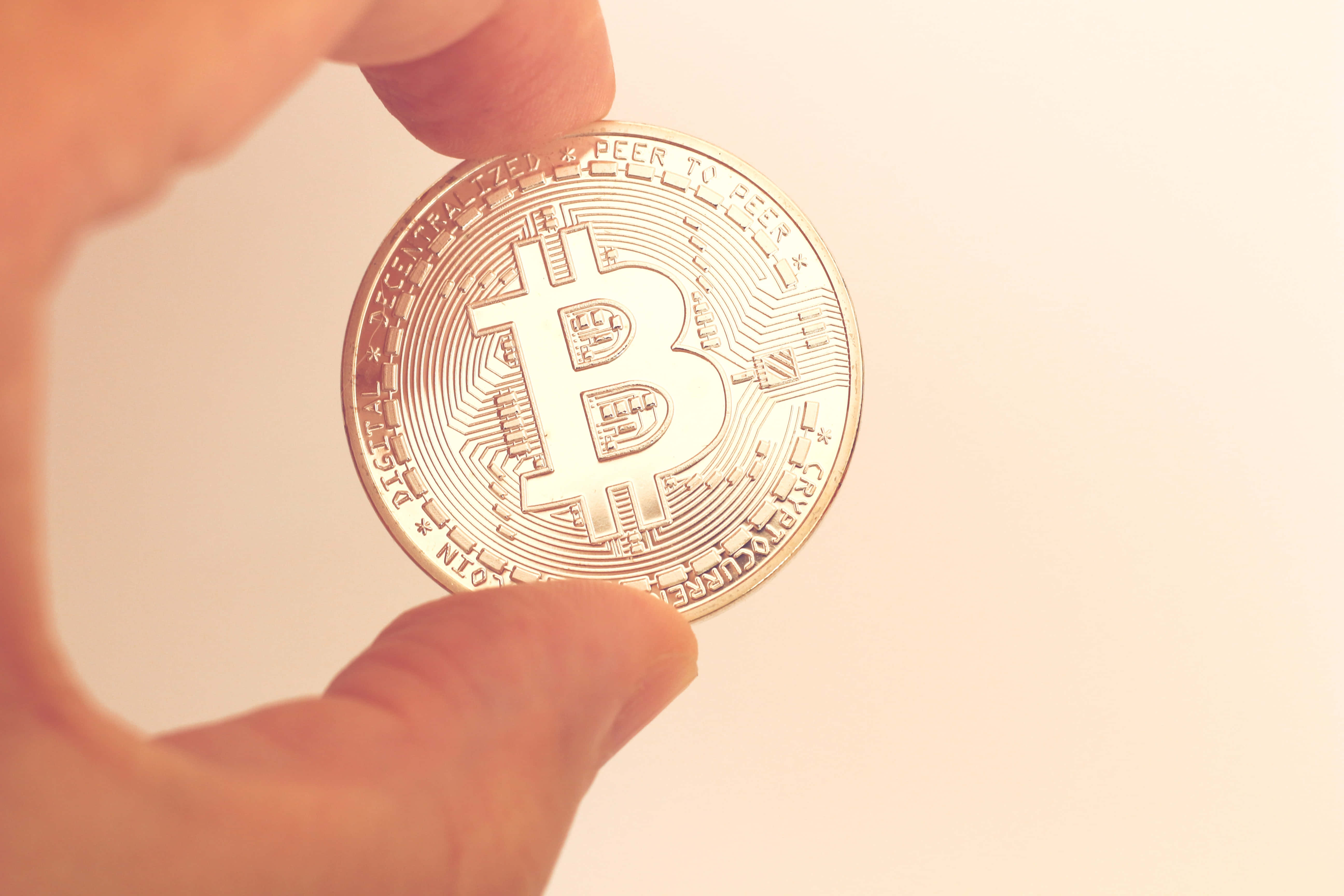 Mining 桌布 壁紙 — 一隻手在柔和溫暖的背景前握著一枚閃亮的金色比特幣硬幣。