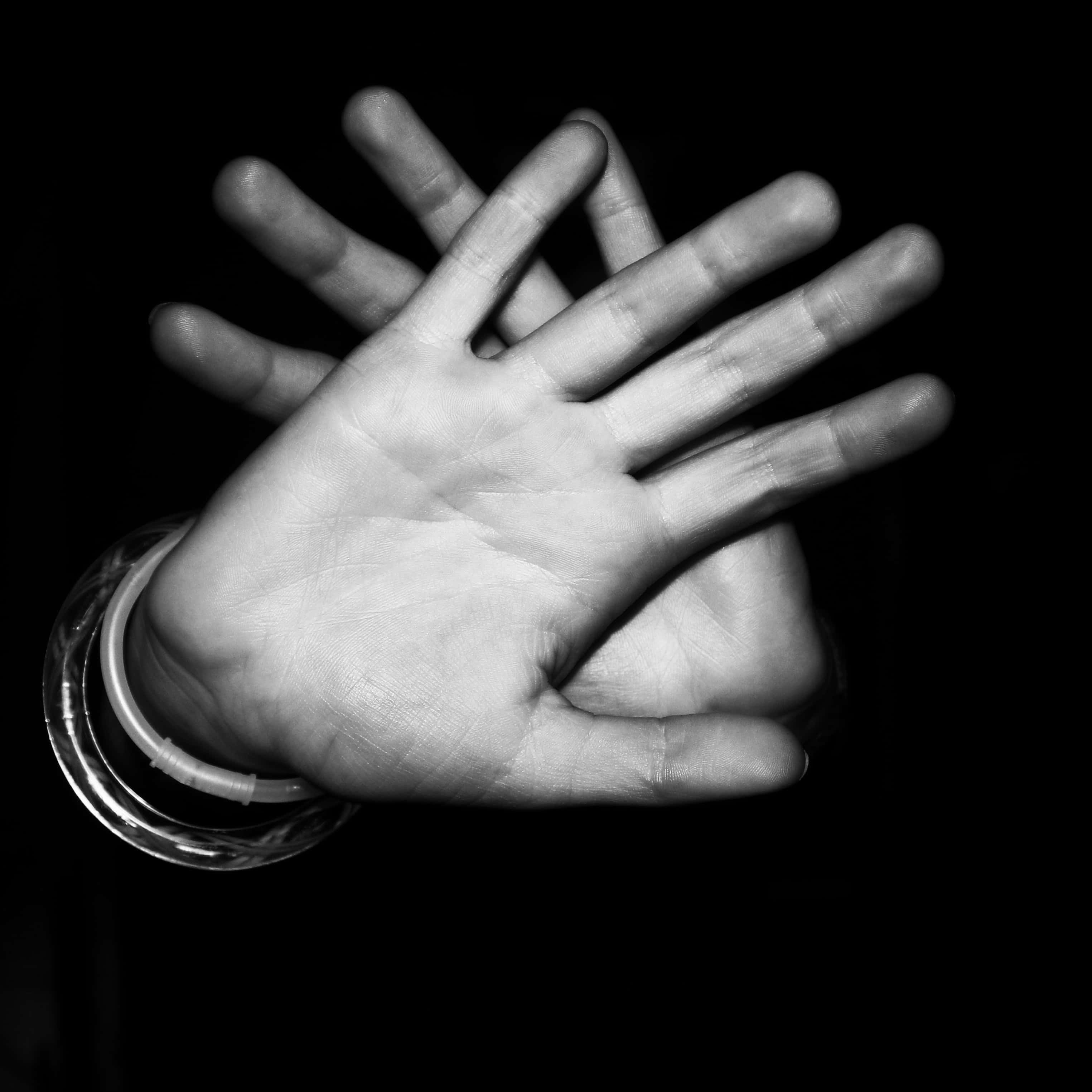 hands 桌布 壁紙 — 一隻手在深色背景下張開手指的黑白特寫，飾有玻璃手鐲。