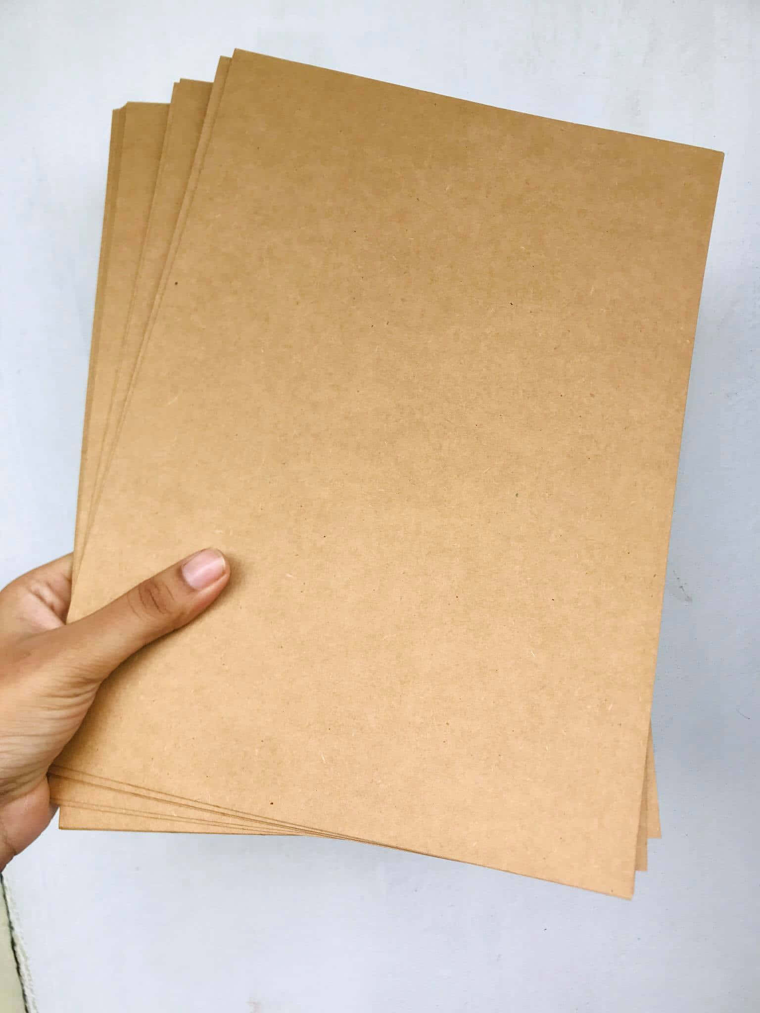 Sheet 桌布 壁紙 — 一隻手在潔白背景前拿著一疊整齊的純棕色牛皮紙。