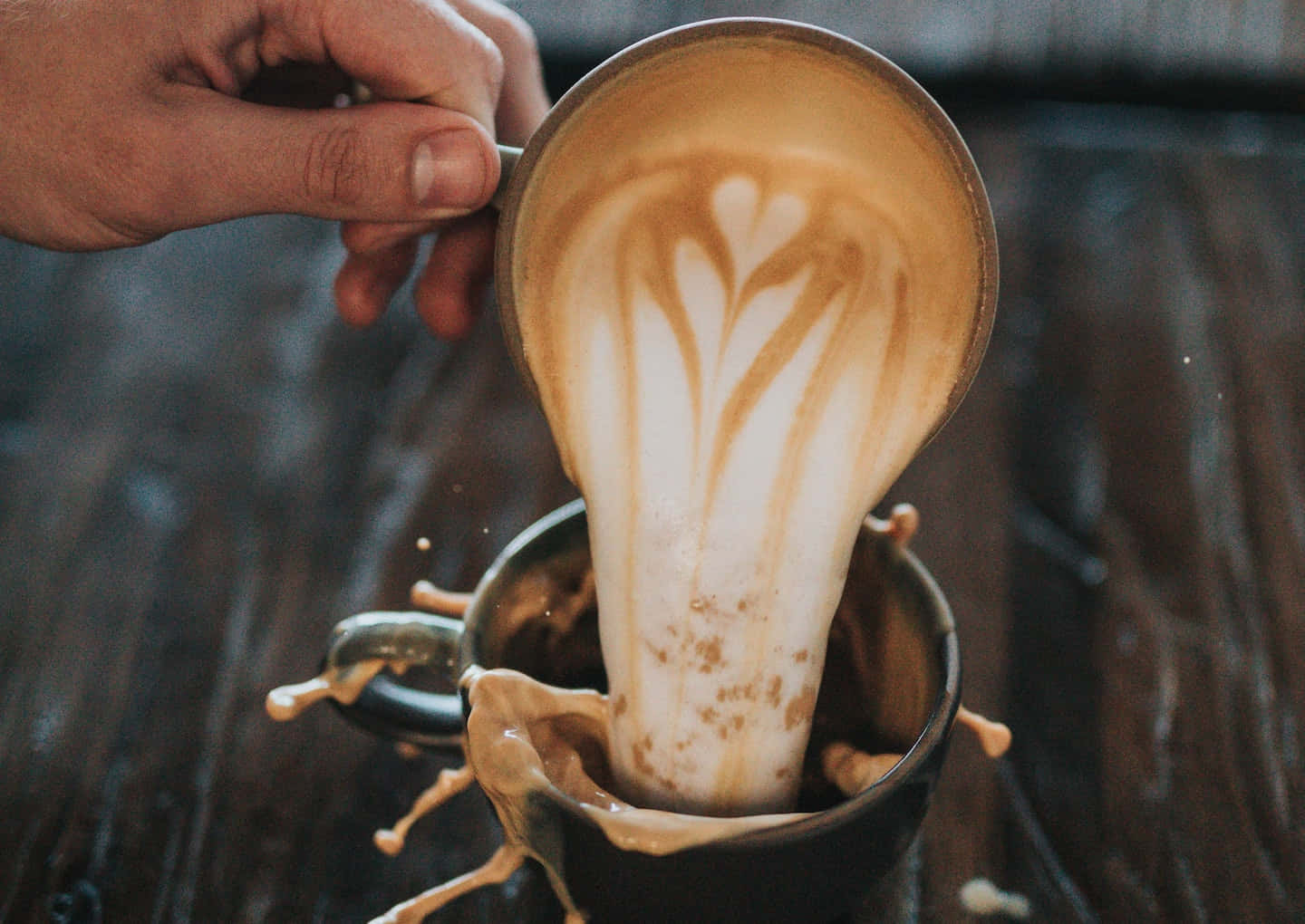 Milk And Coffee 桌布 壁紙 — 一隻手將帶有心形圖案的奶油拉花藝術倒入深色馬克杯中，牛奶戲劇性地濺在木桌上。