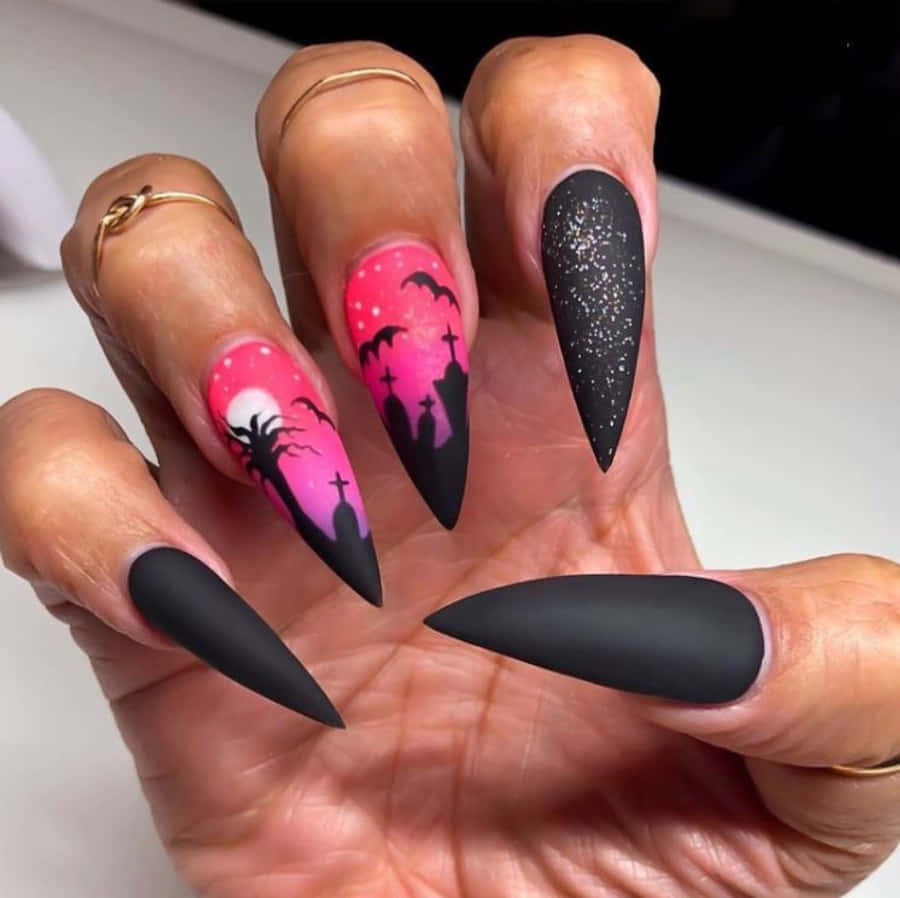 Halloween Nail Art 桌布 壁紙 — 一隻手展示戲劇性的萬聖節主題指甲，帶有粉紅色墓地場景和閃亮黑色指尖，背景為純色。