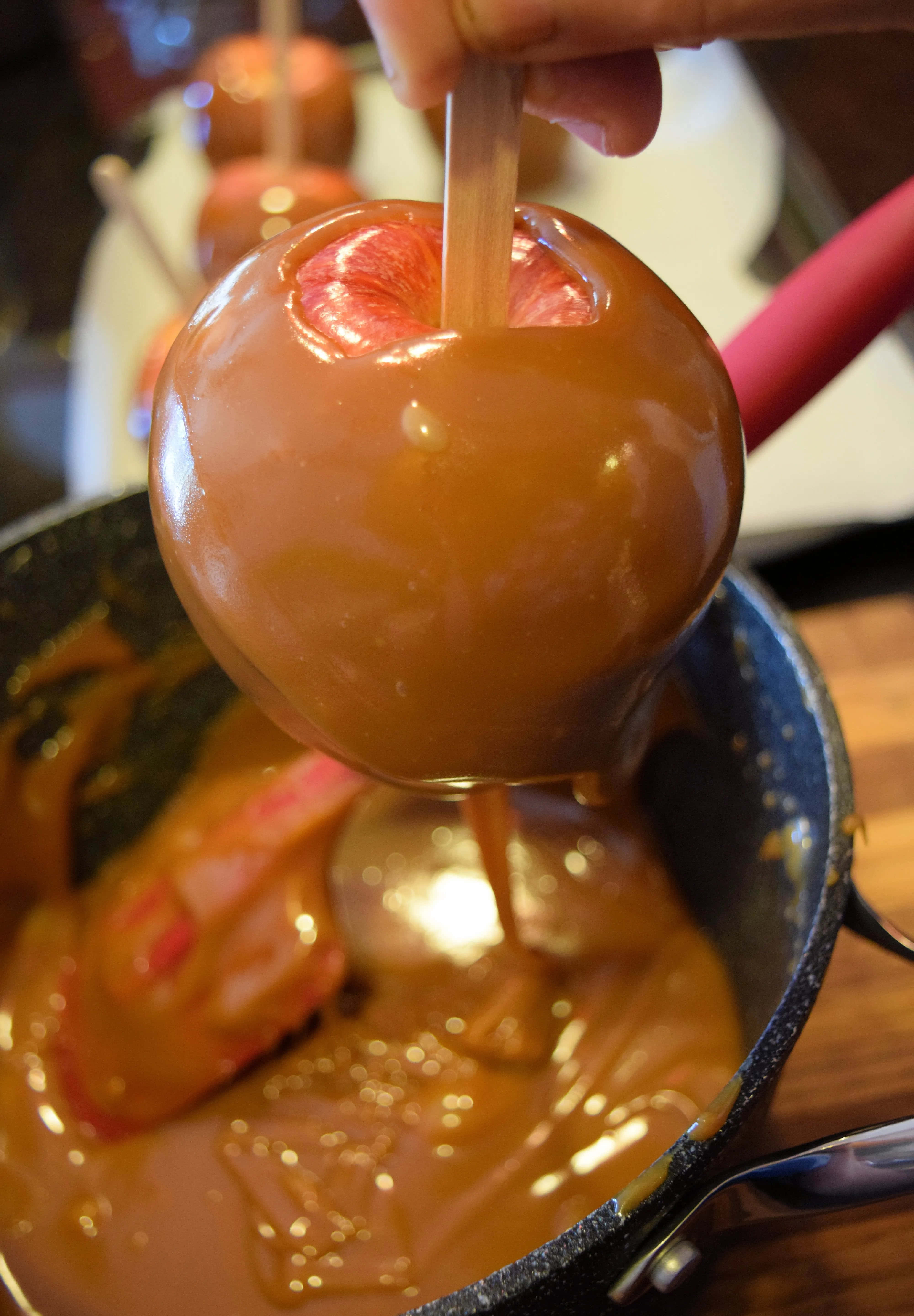 Caramel Apples 桌布 壁紙 — 一隻手從冒泡的金黃色焦糖醬鍋中拿起一個閃亮的焦糖蘋果。