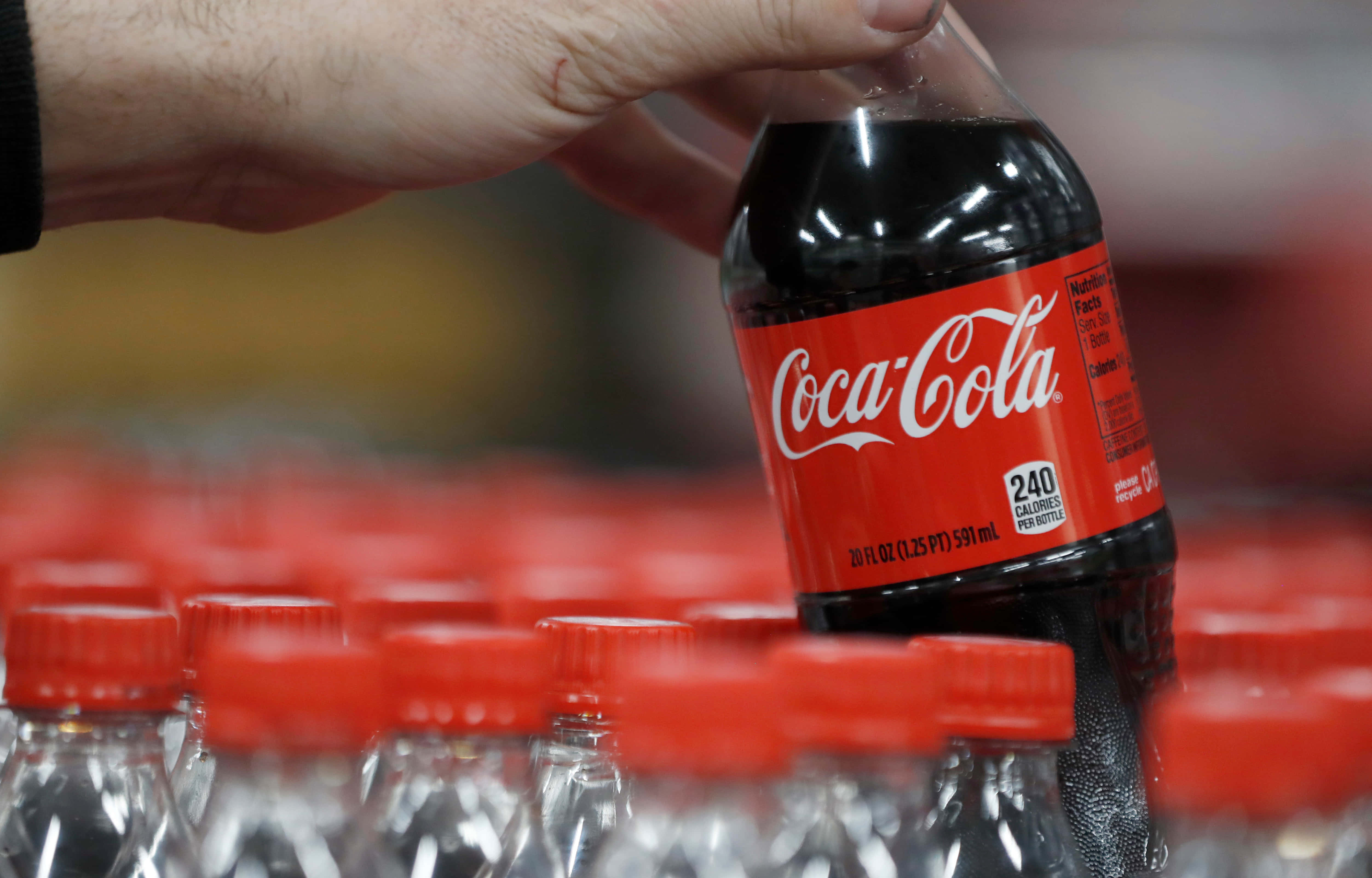 coca cola 桌布 壁紙 — 一隻手從商店貨架上拿起一支冰凍的可口可樂瓶，貨架上擺滿了相同的瓶子。