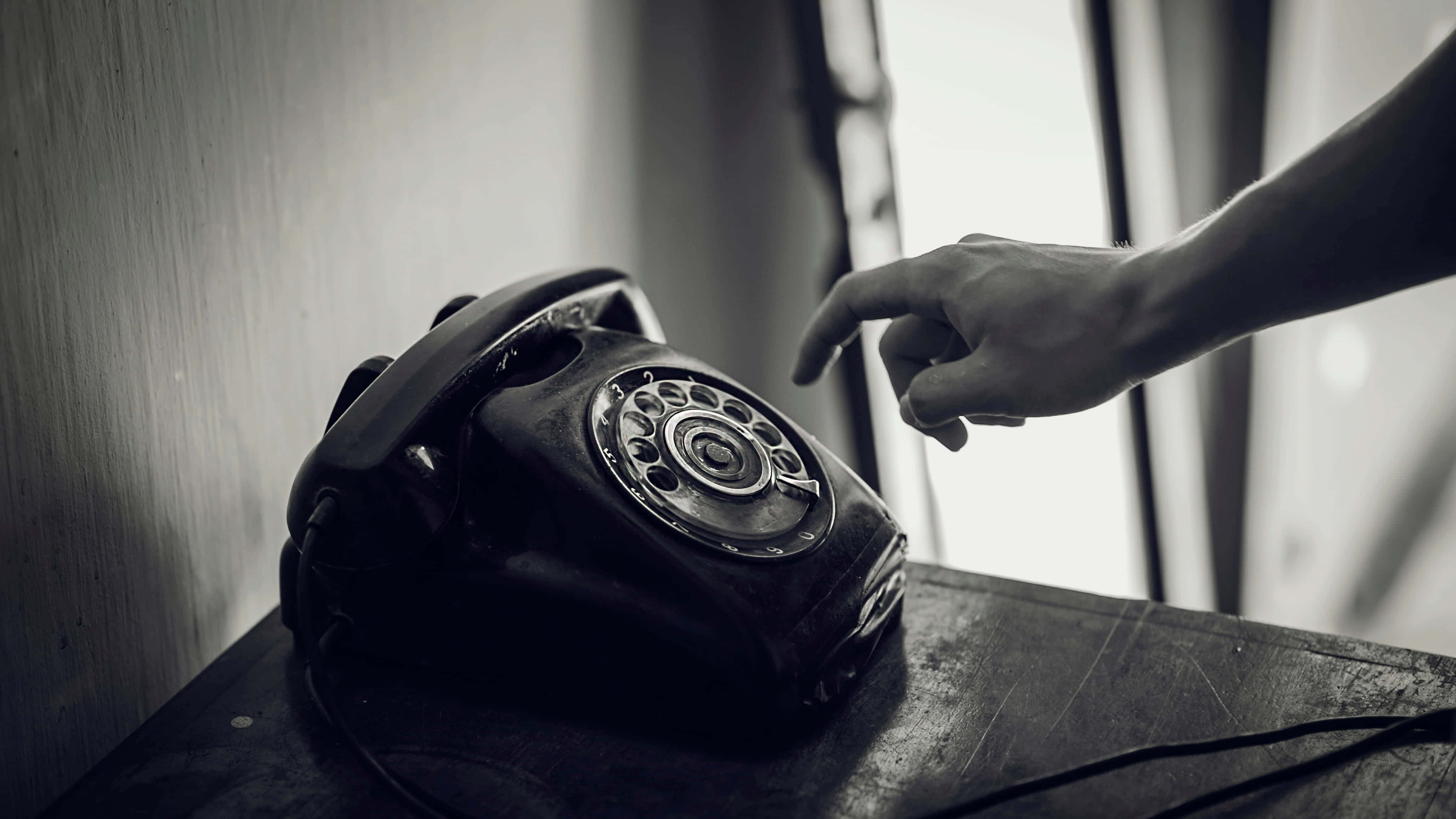 Phone Call 桌布 壁紙 — 一隻手懸浮在木質表面上的復古轉盤電話上方，處於單色設定中。