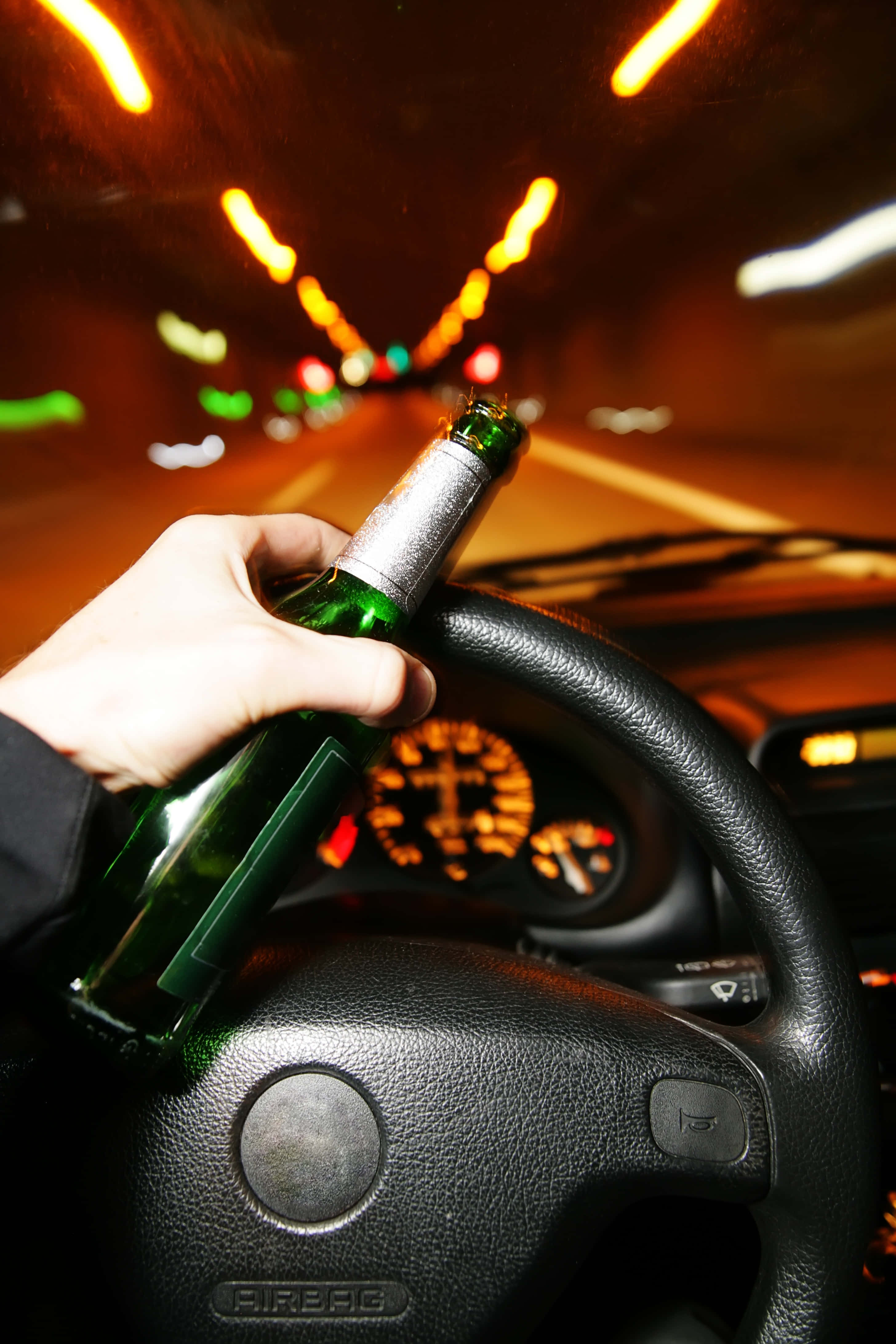 醉咗 桌布 壁紙 — 一隻手抓住汽車軚盤上的綠色啤酒瓶，模糊的隧道燈光以溫暖的橙色色調掠過。