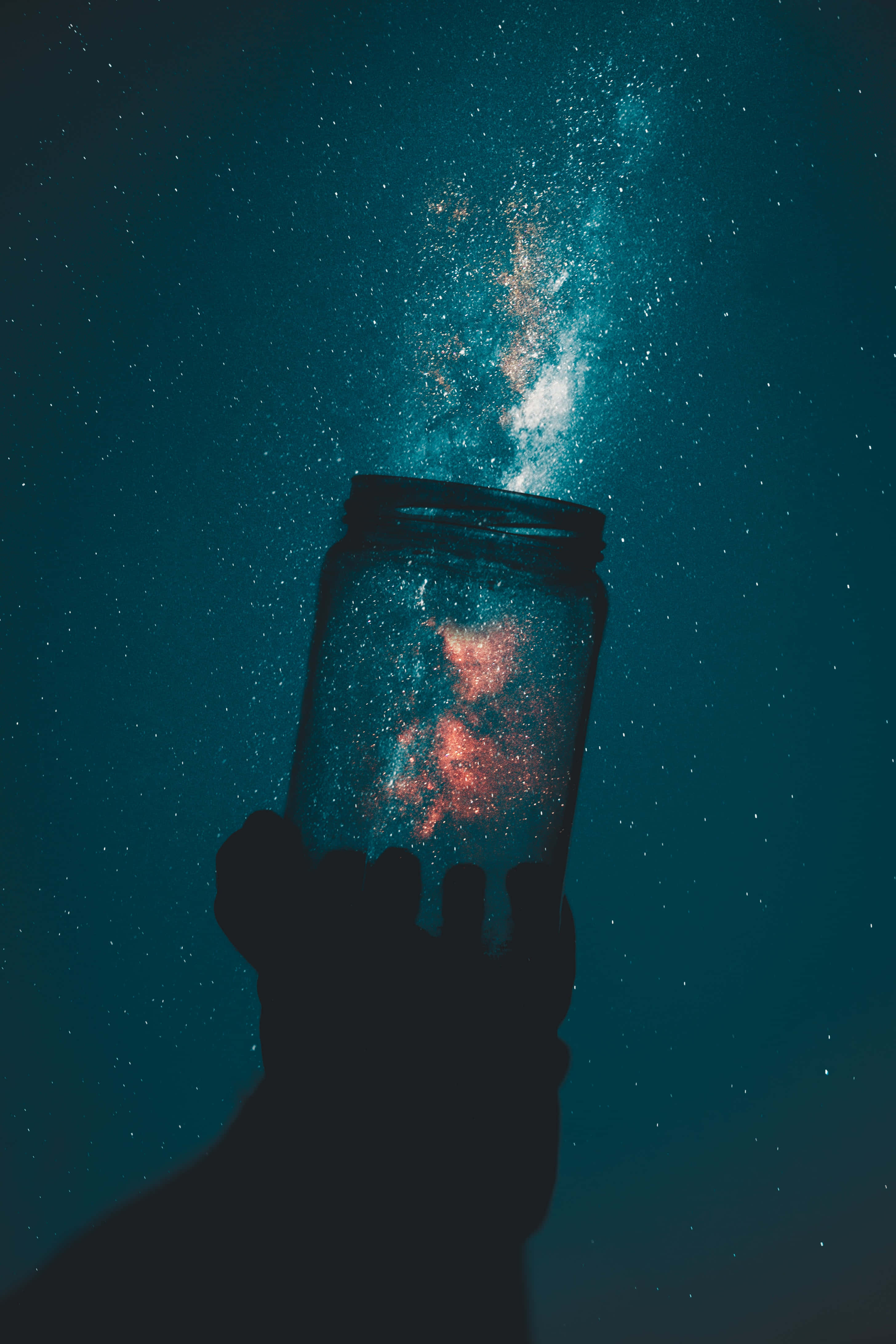 Kawaii Galaxy 桌布 壁紙 — 一隻手拿著一個罐子，向繁星點點的藍綠色夜空釋放出閃閃發光的宇宙塵埃。