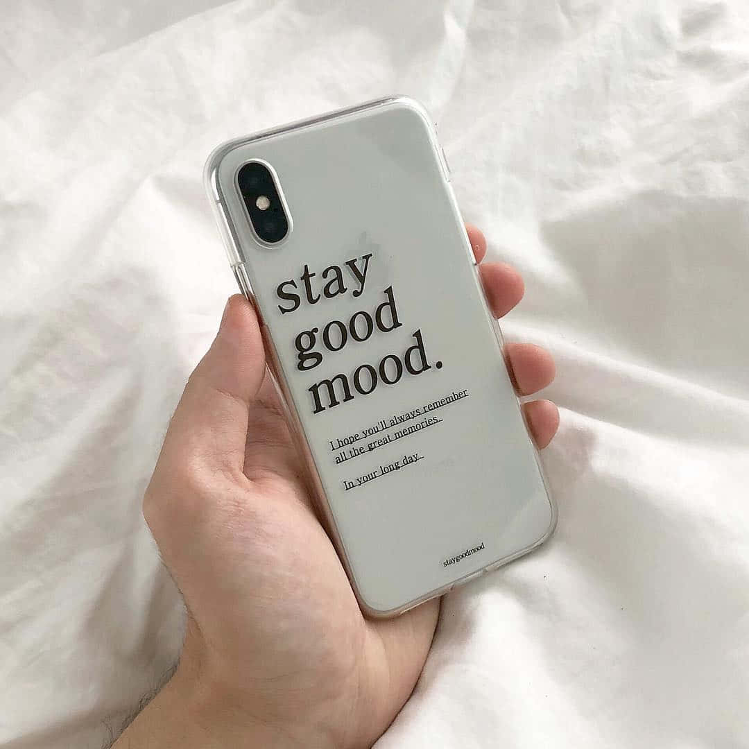 iPhone風格壁紙 桌布 壁紙 — 一隻手拿著一個透明手機殼，上面有 'stay good mood' 字樣，背景是柔軟的白色床單。