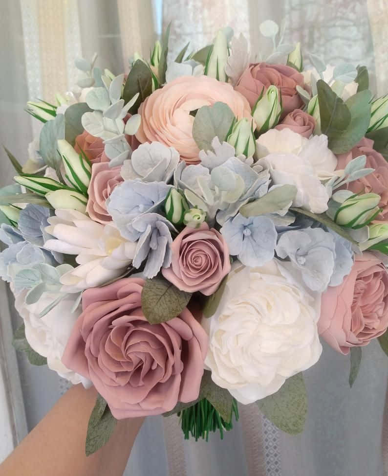 Roses Wedding 桌布 壁紙 — 一隻手拿著一束豐富的粉彩粉紅、白色和藍色花朵，搭配綠葉，背景是柔軟的窗簾。