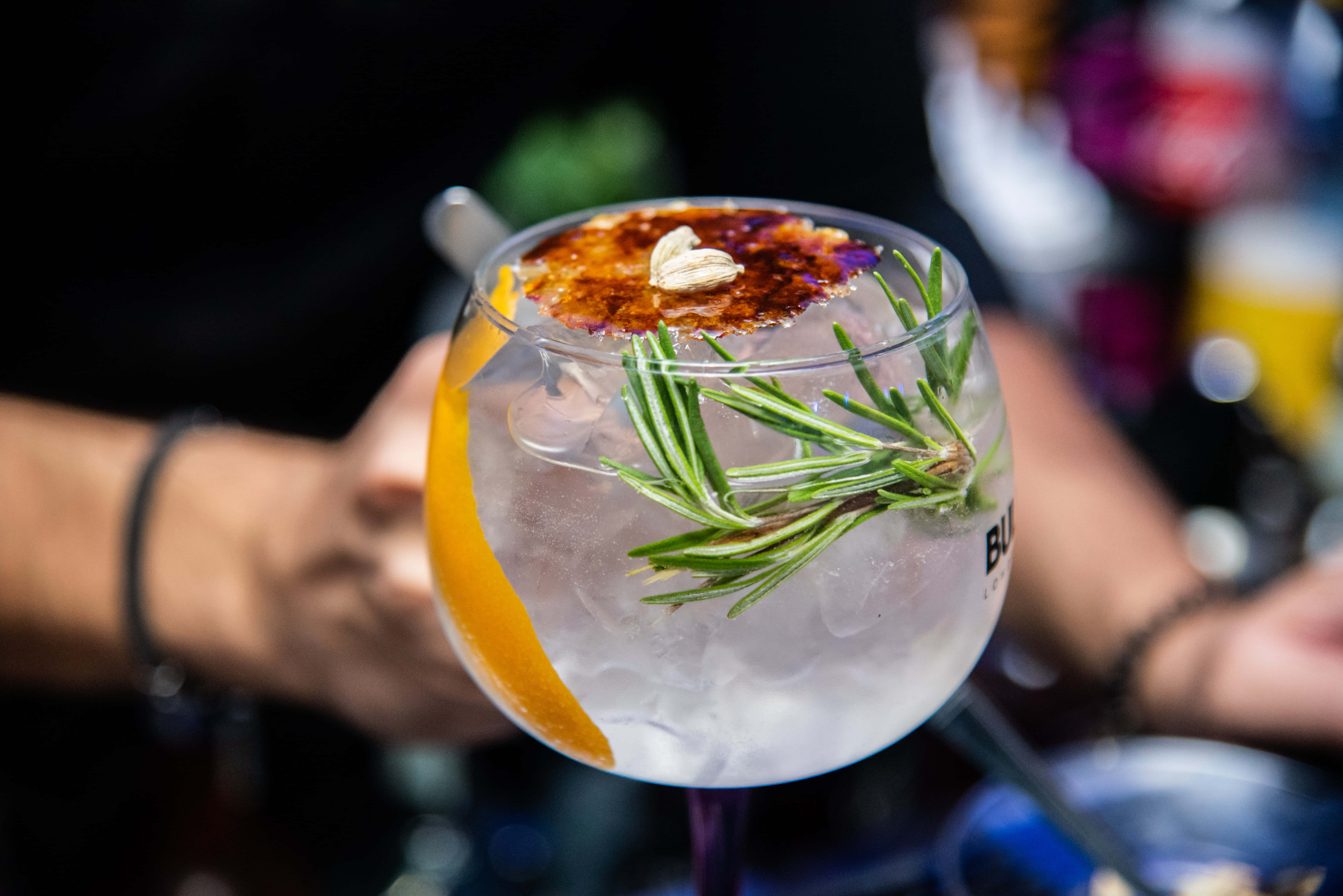 Summer Drinks 桌布 壁紙 — 一隻手拿著一杯冰凍的氈酒雞尾酒，飾以迷迭香橙片和焦糖。