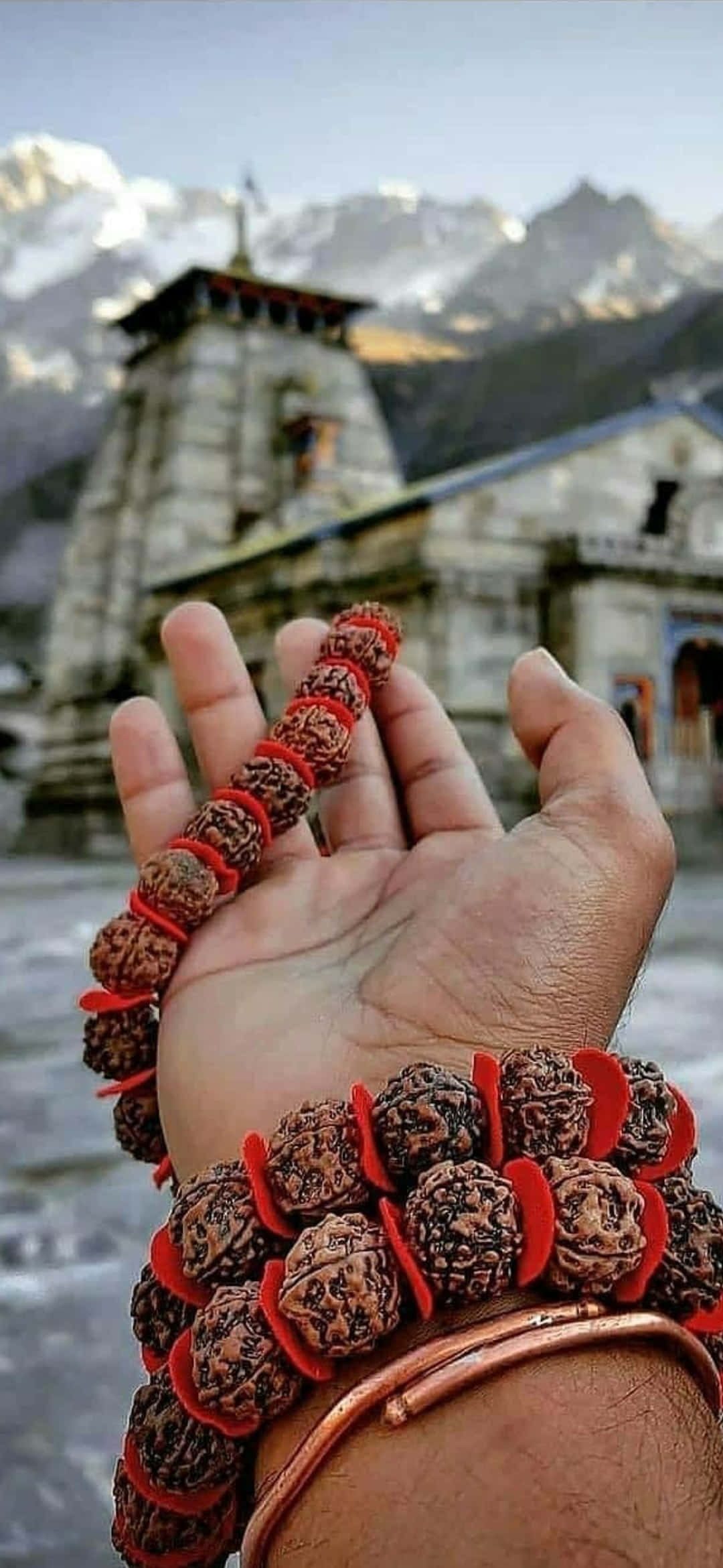 Kedarnath 桌布 壁紙 — 一隻手拿著一條紅繩的 Rudraksha 念珠，背景是石廟和白雪覆蓋的喜馬拉雅山峰。